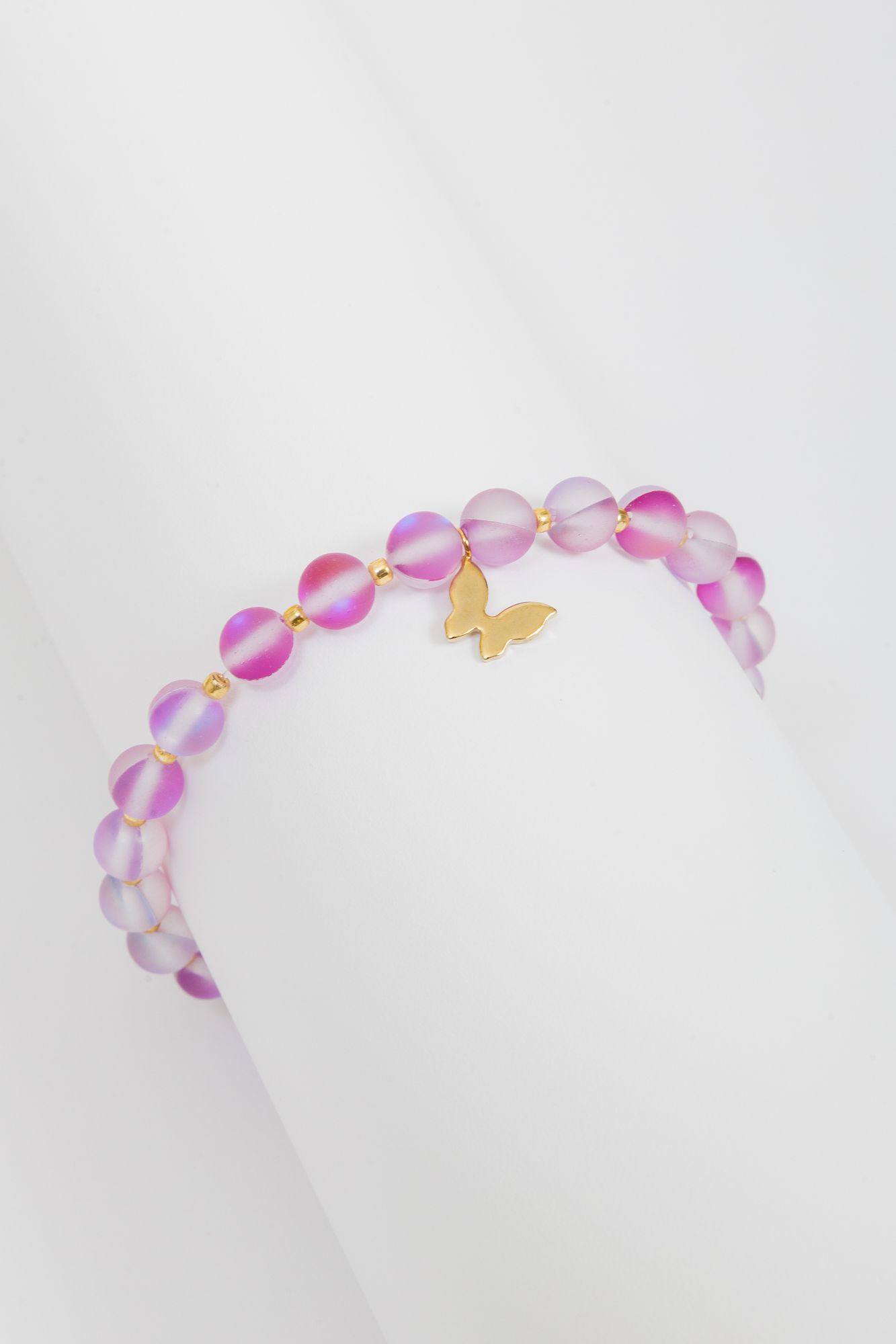 Pink iridescent beaded bracelet with small gold butterfly charm on white background.