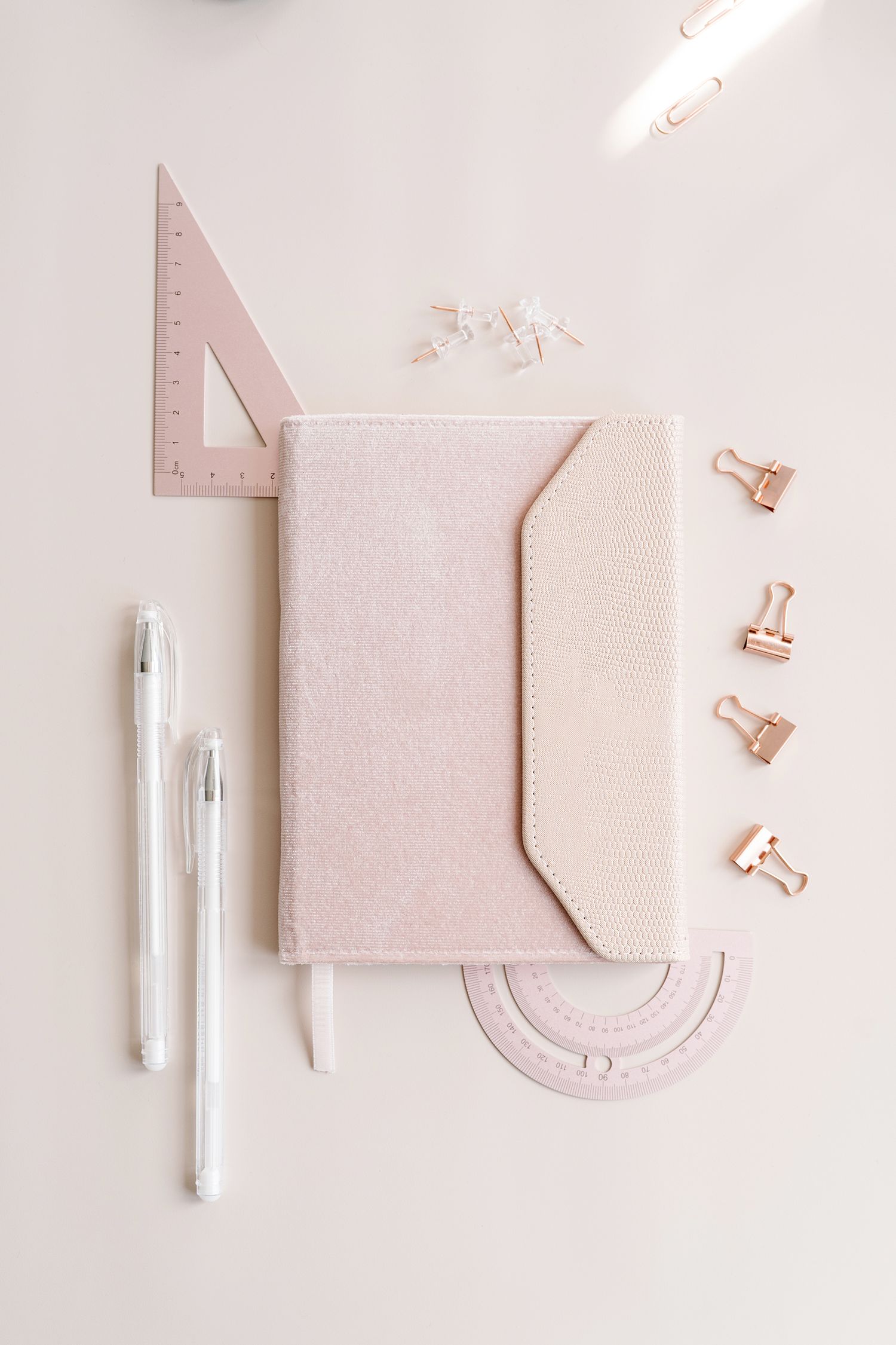 Pink geometric stationery items and rulers arranged on white surface.