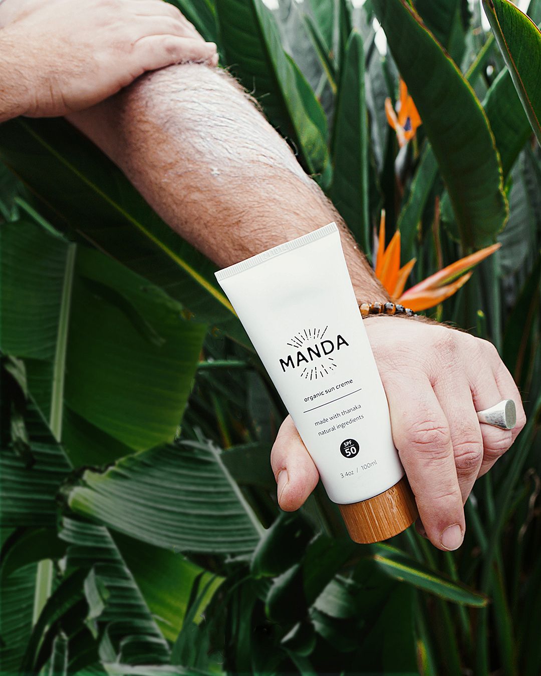 Product shots of Manda skincare bottle against tropical green leaves and orange flowers.