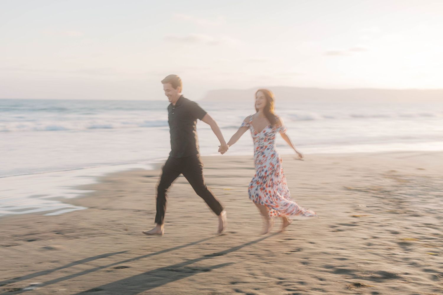 Couple chasing each other playfully across the sand at dusk.