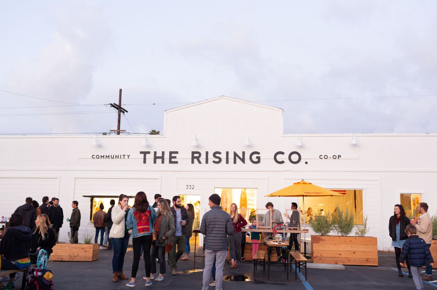 Small coffee shop storefront with white walls and a cross on top stands against blue skies during sunrise or sunset.