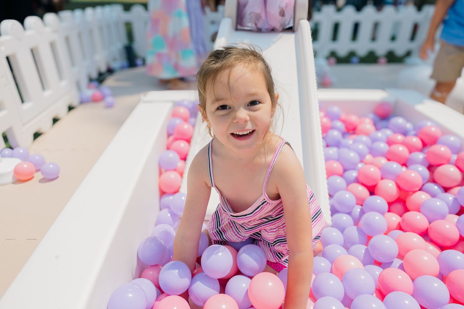 Party scene with pink and purple balls in a white fenced play area.