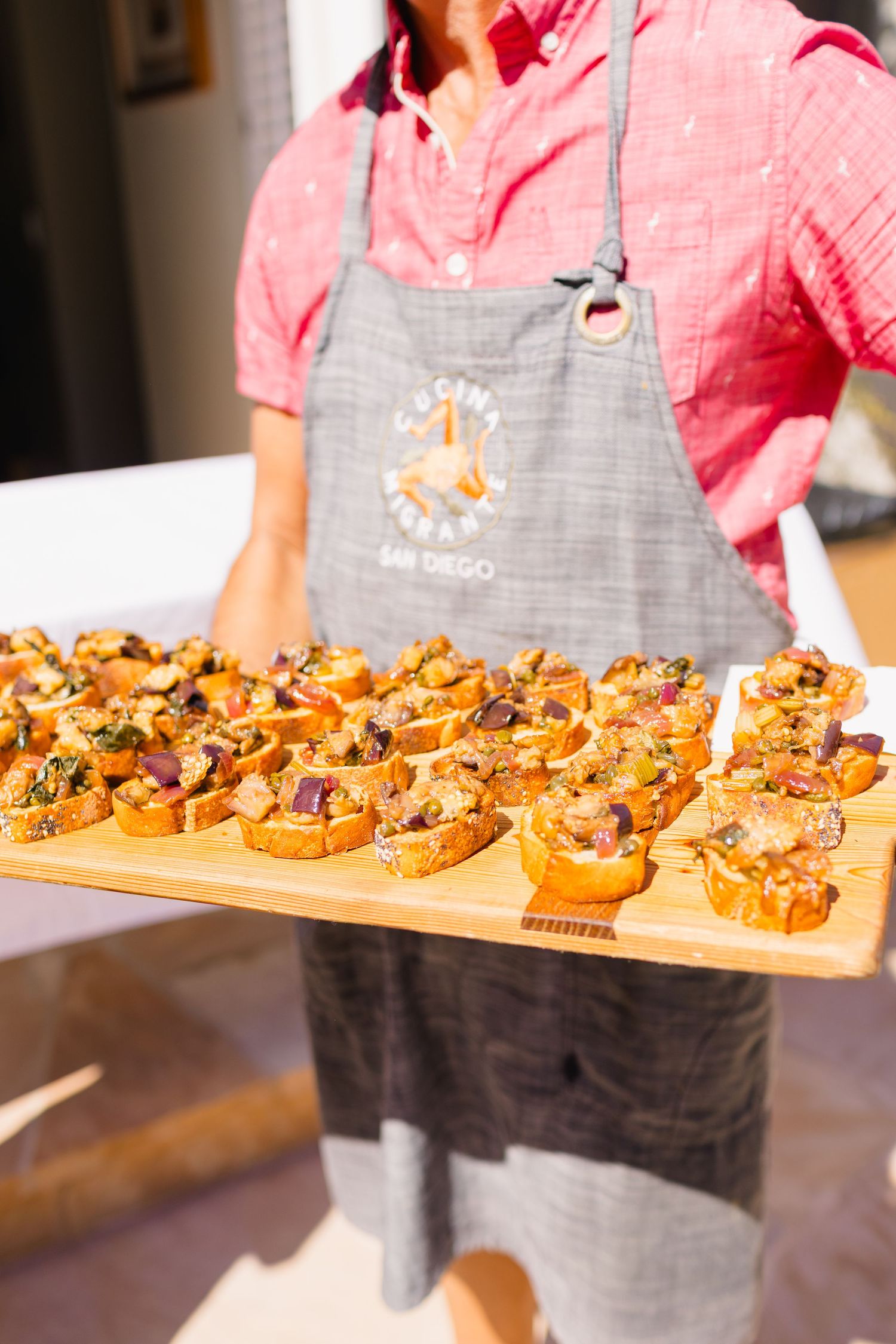 Wooden serving board displaying rows of beautifully arranged appetizers topped with garnishes.