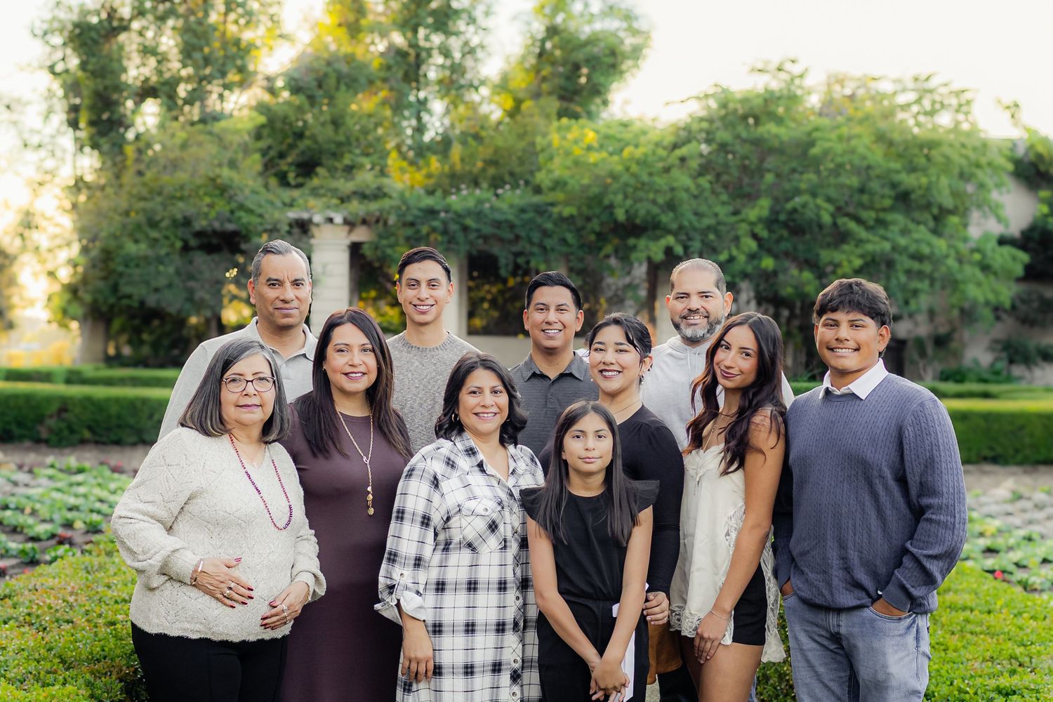 Multi-generational family gathers outdoors for a group photo in a lush garden setting at sunset.