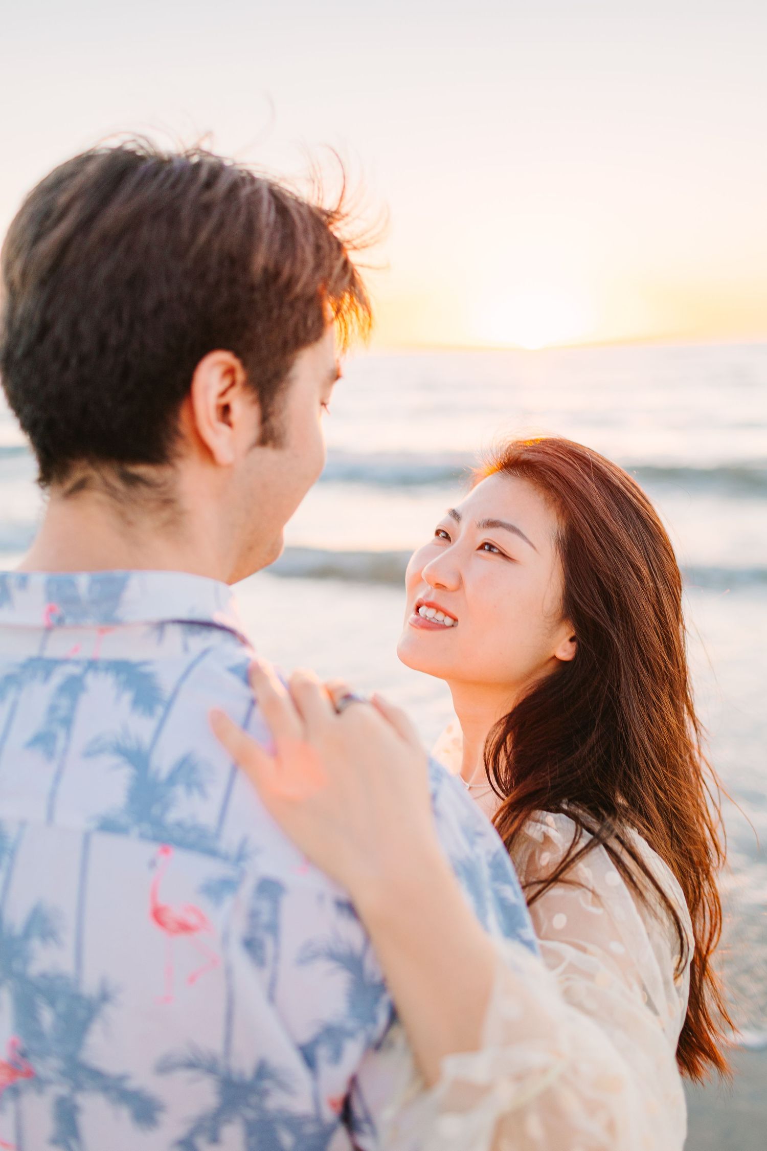 Playful couple laughs together during sunset beach photoshoot wearing coordinated outfits.
