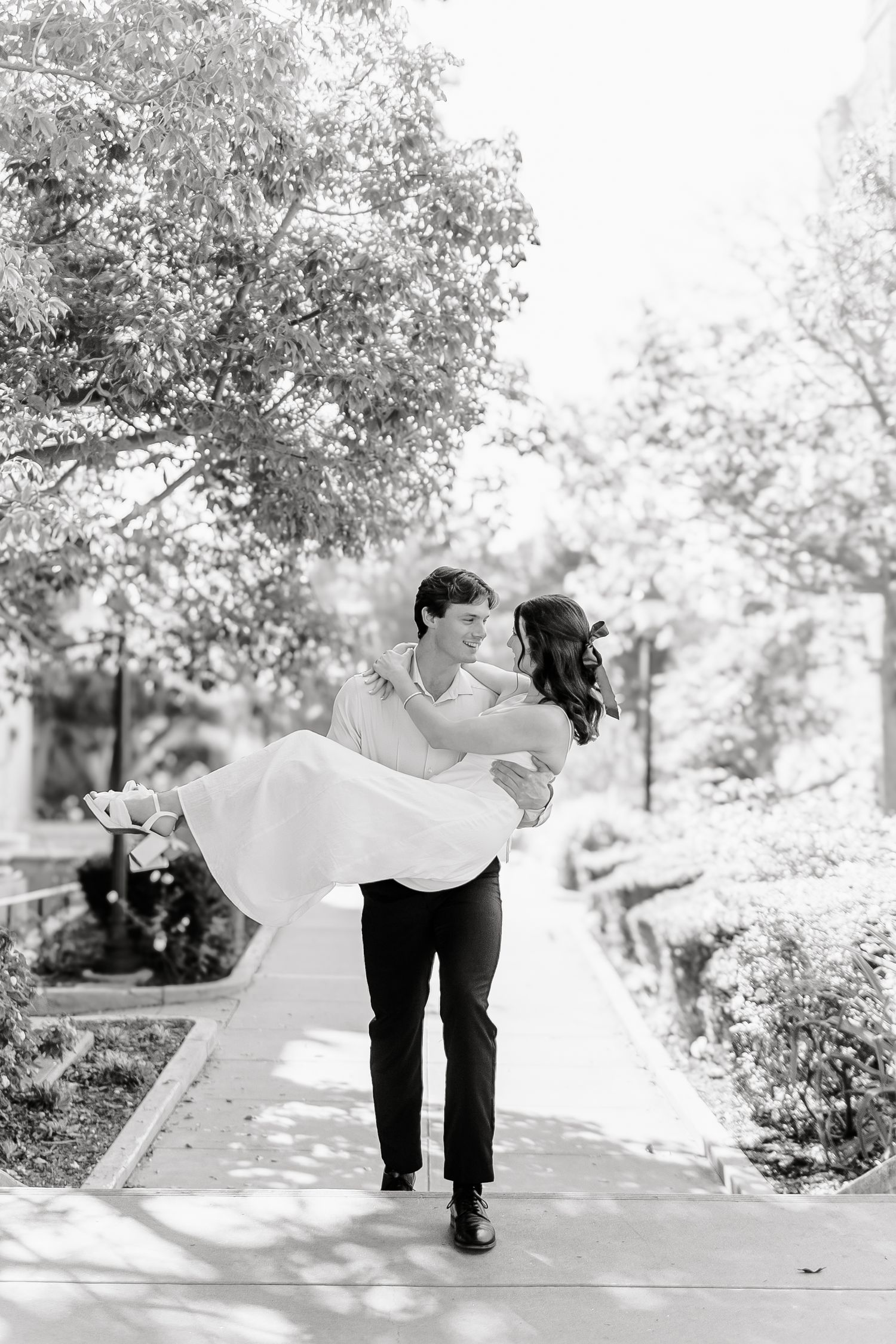 A romantic black and white wedding photo of a couple on a garden pathway with overhanging trees.