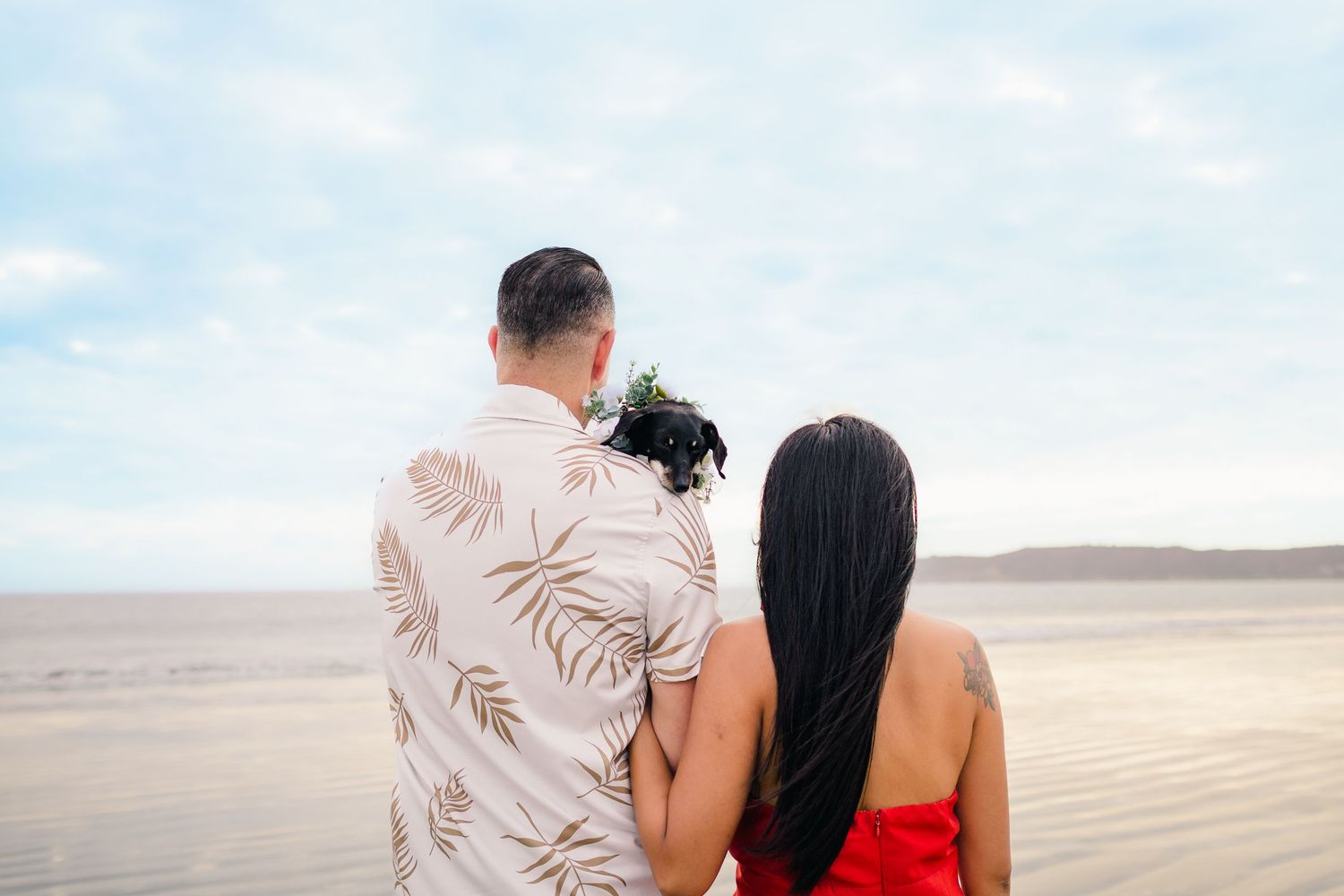 Couple walking hand in hand along a sandy beach during sunset with mountains in the background.