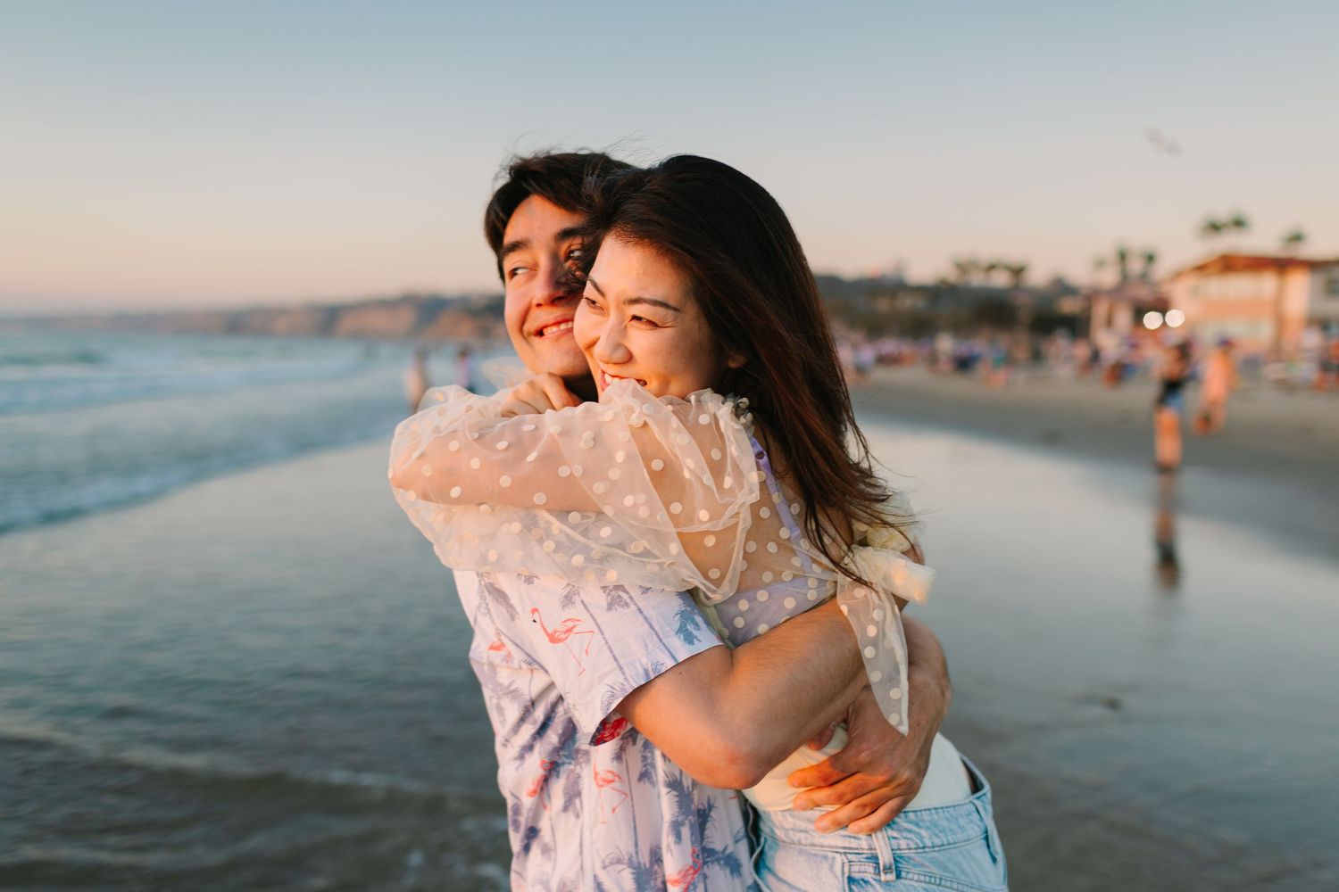 Couple shares intimate moment on sandy beach with ocean waves and sunset in background.
