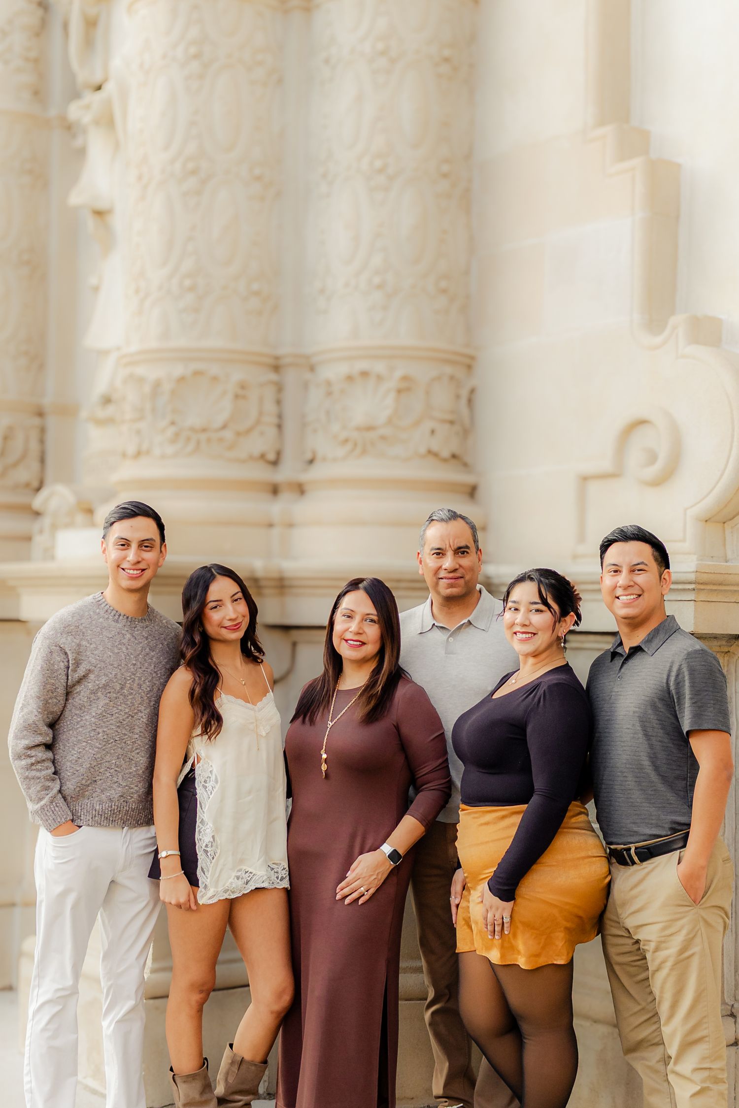 A group of people standing together and smiling in front of a white ornate architectural backdrop.