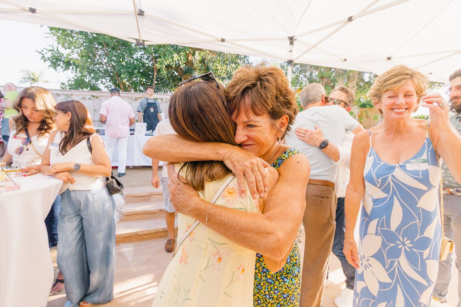 Happy guests embracing and celebrating at a festive outdoor gathering under a white canopy.
