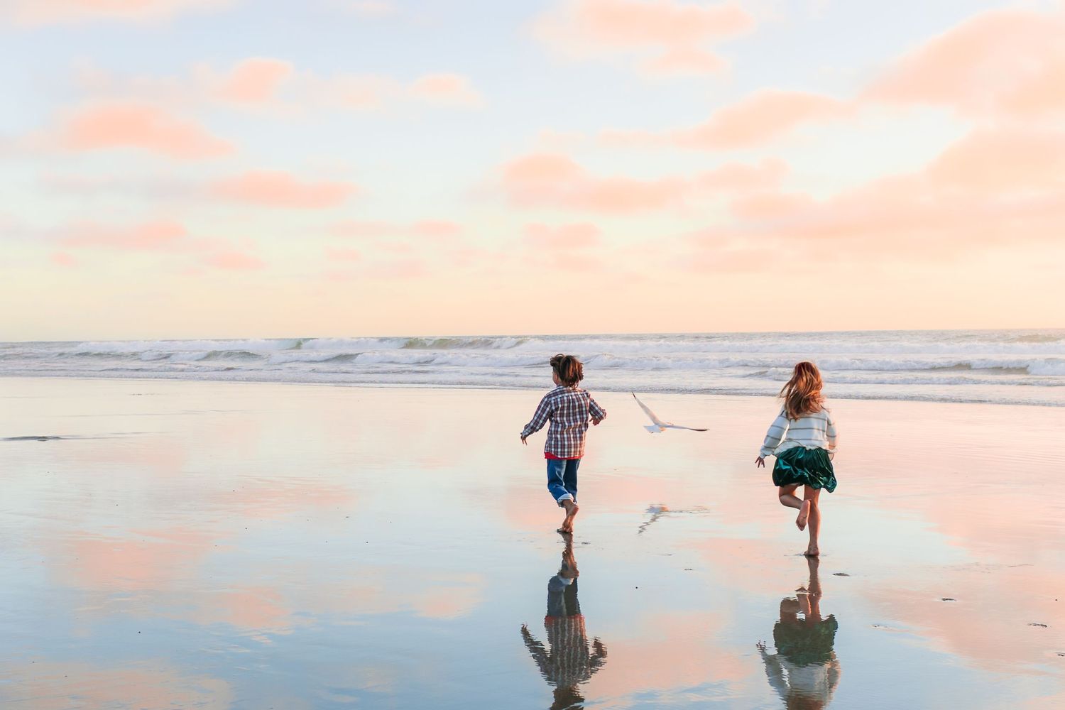 Silhouettes of people walking and playing on a beach at sunset with golden light reflecting off the water.