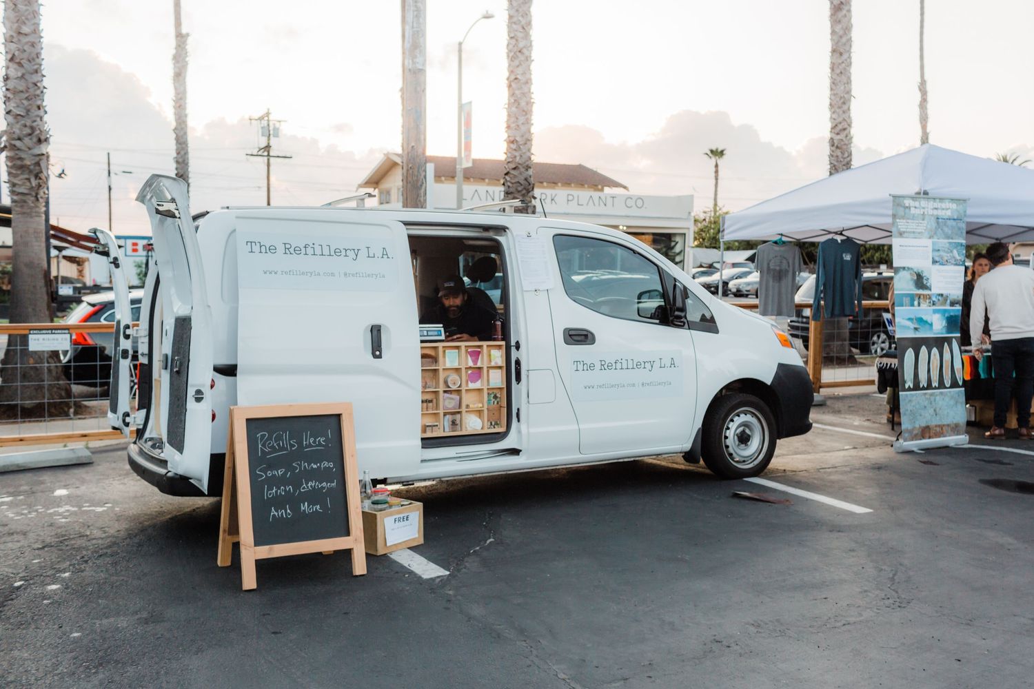 White food truck parked on street with chalkboard sign and other mobile vendors visible in neighborhood setting.
