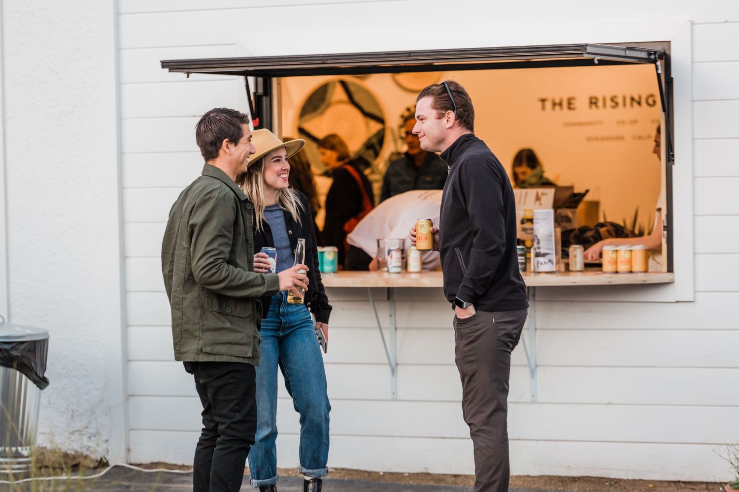 People gathered in front of a restaurant window with drinks and casual conversation during an evening social event.