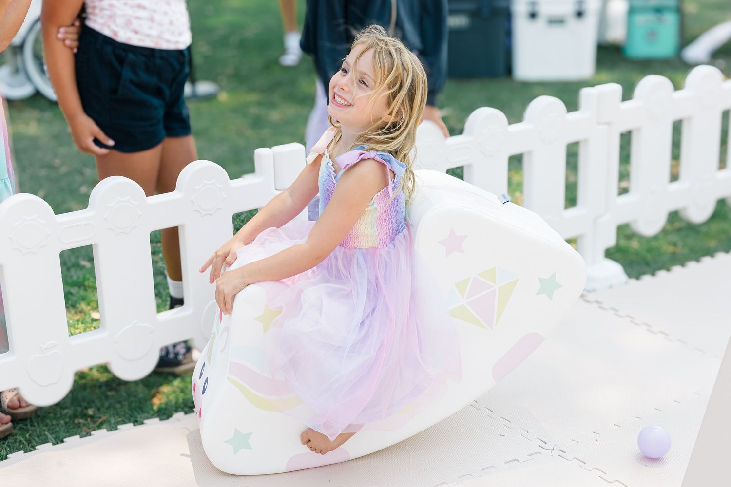 White and pink themed party setup with decorative elements and fencing outdoors.