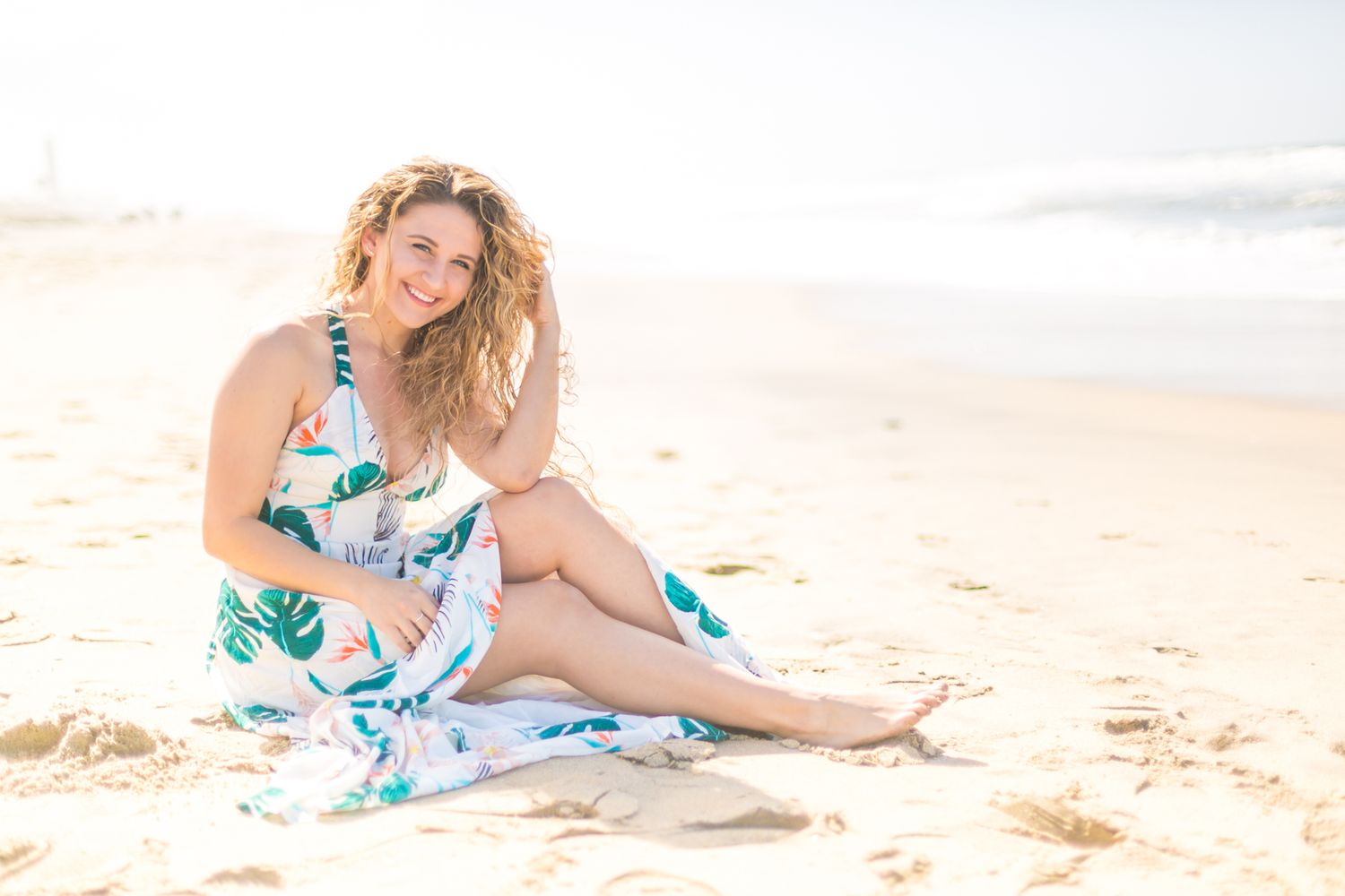 Beautiful beach photoshoot at sunset with a floral dress against golden skies and ocean waves.