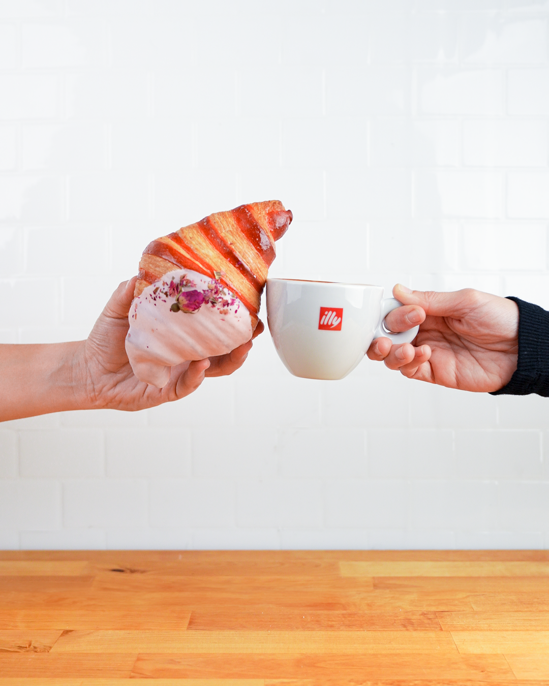 Hands passing white illy coffee cup across wooden table surface.