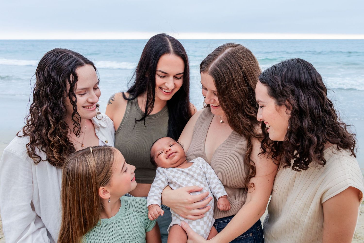 A group gathers around a smiling baby on the beach.