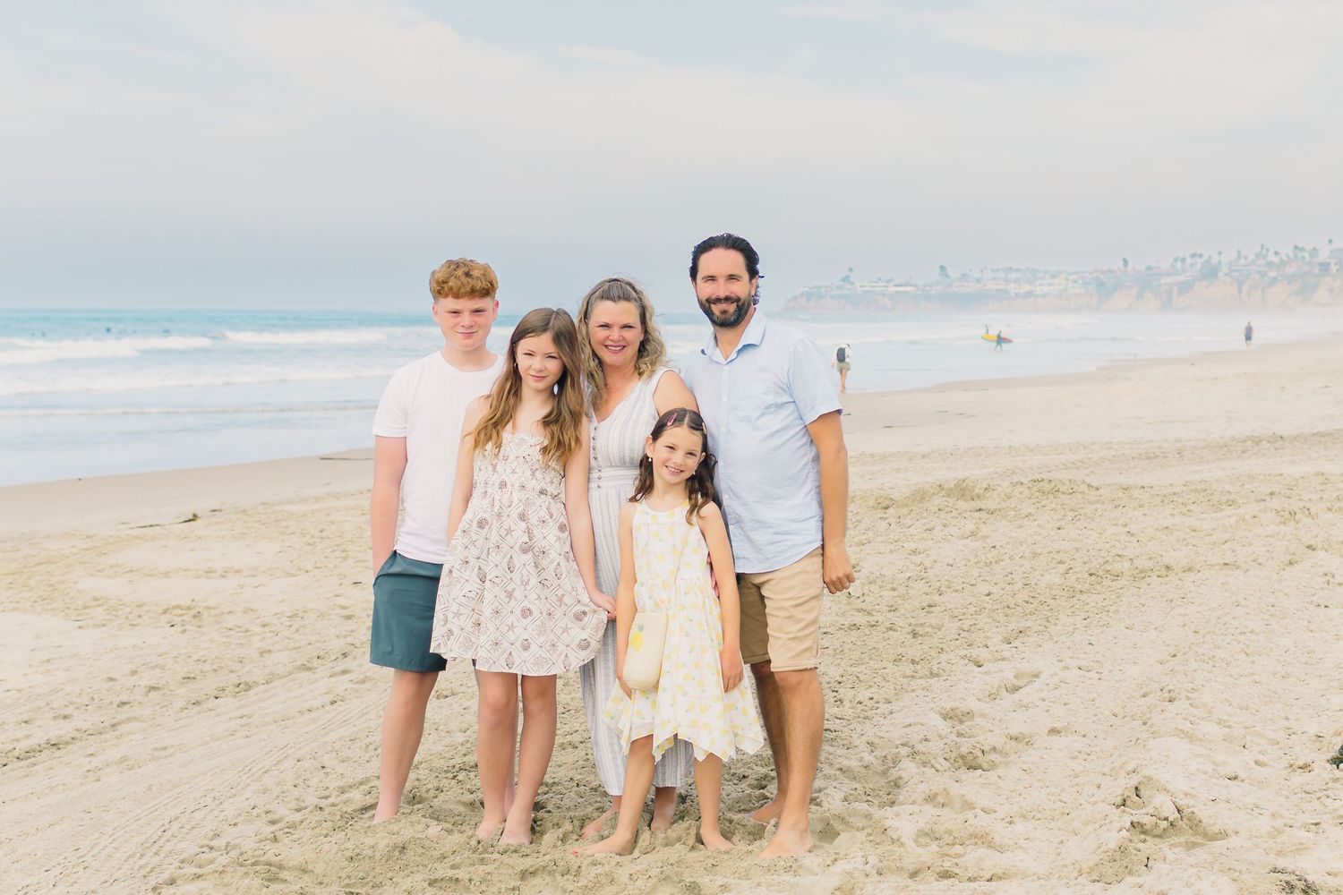 Family enjoying a sunny day together at the beach with ocean waves and blue sky in the background.