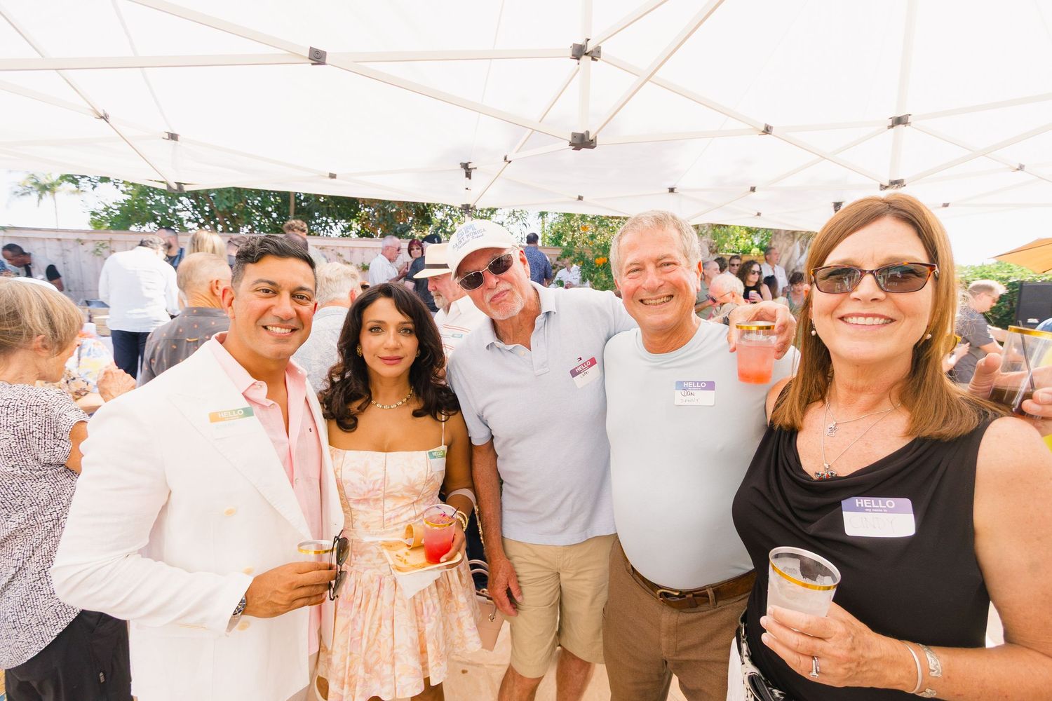Party attendees mingling under a white canopy tent during a daytime social gathering.