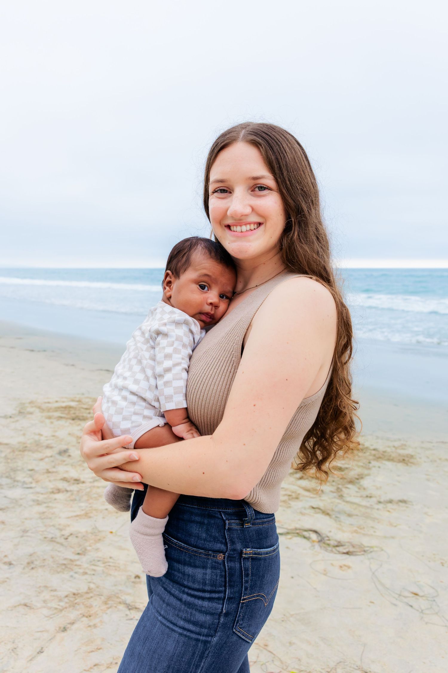 Person holding small infant on beach with ocean waves in background.