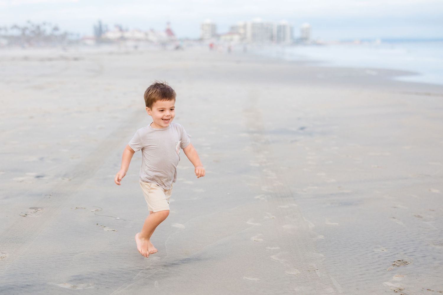 A young child runs joyfully along the beach shoreline during an overcast day.