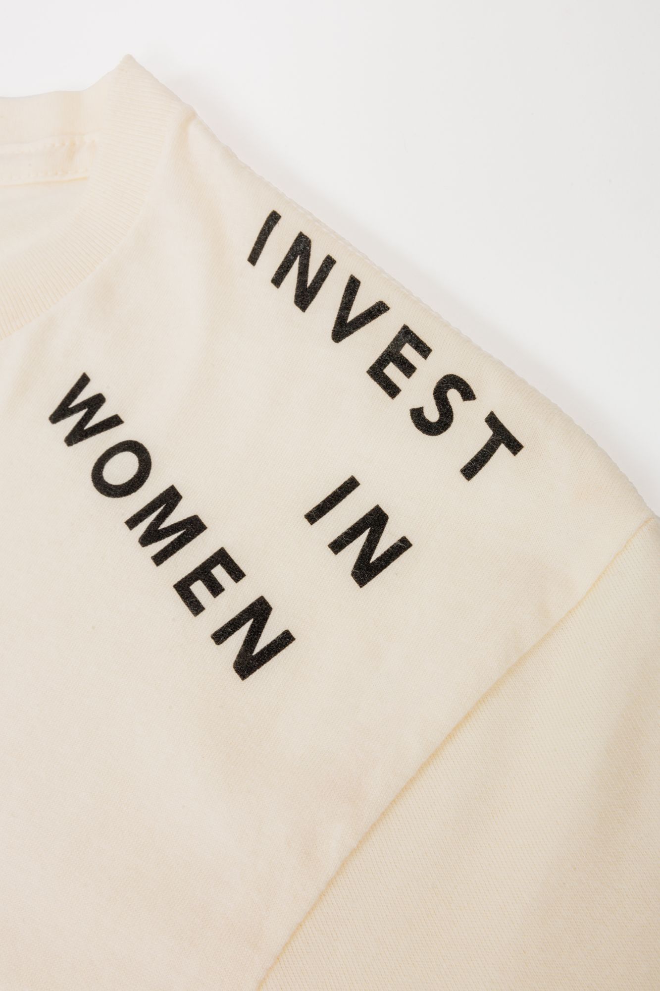 Close-up of cream-colored fabric with bold black text reading 'INVEST IN WOMEN'.