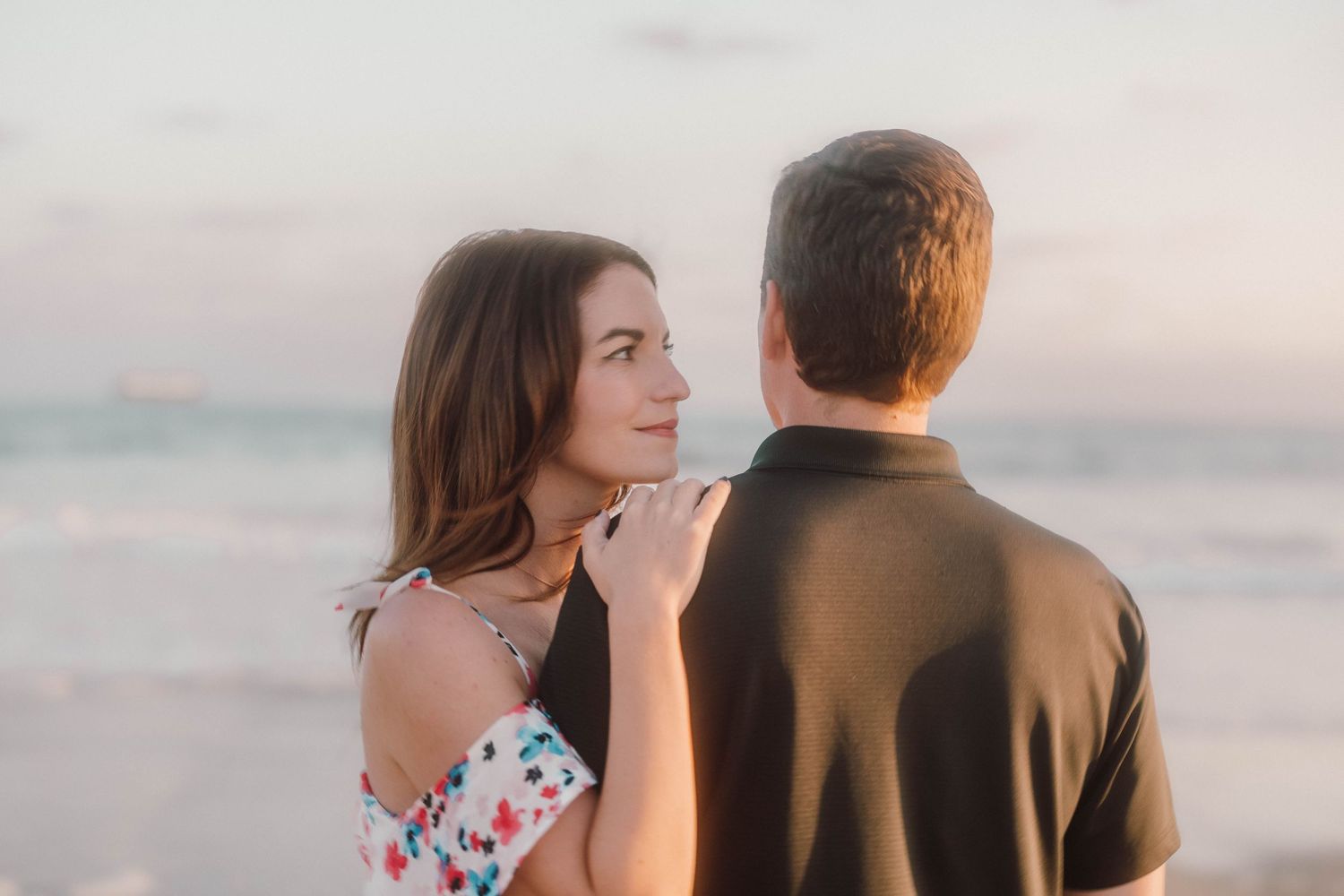 Tender embrace between couple on beach during sunset with soft pastel sky.
