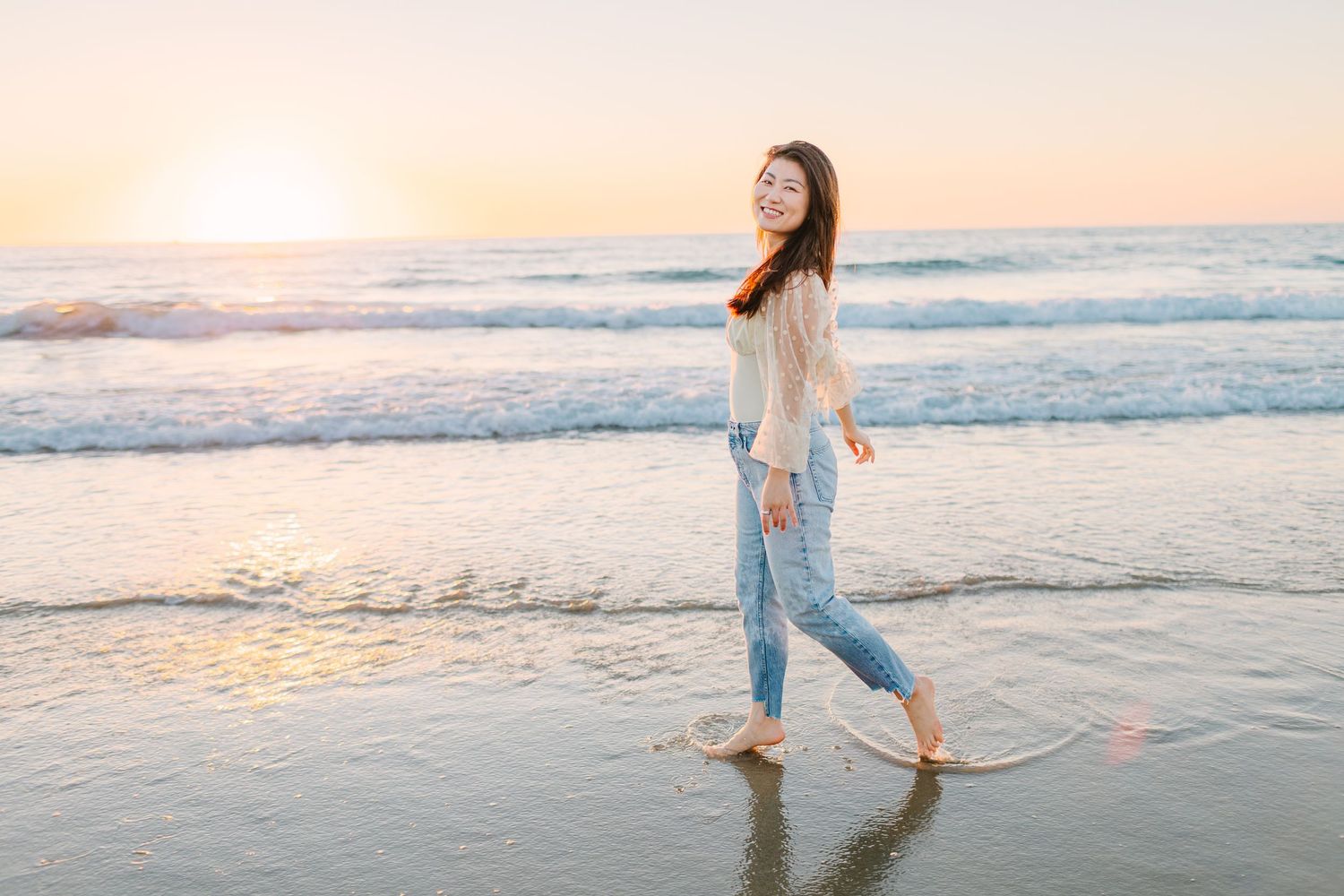 Person walking barefoot along beach shoreline during golden sunset with waves in background.