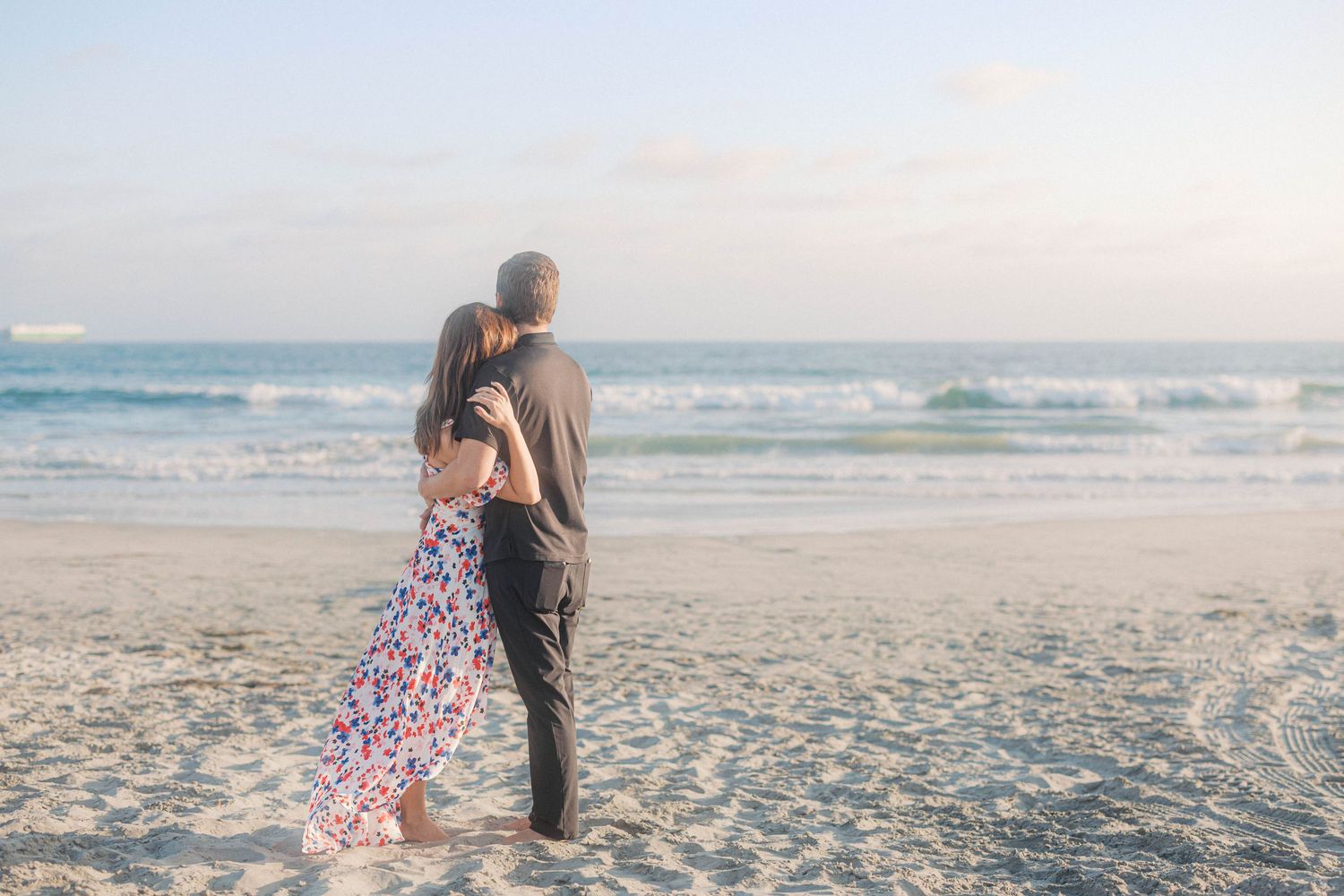 A couple embraces on a wide sandy beach with the ocean horizon behind them.