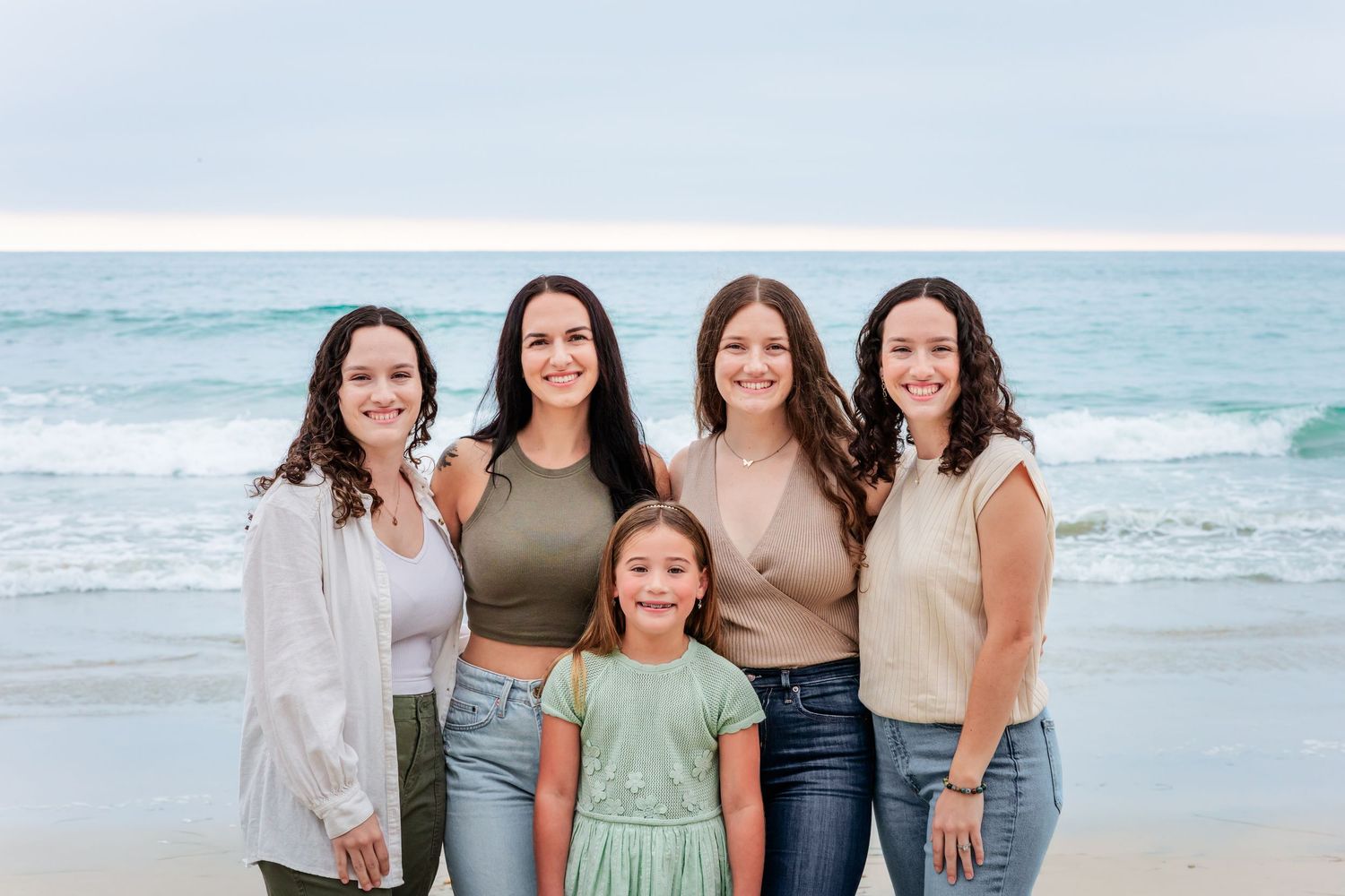 Five people stand together on beach with waves crashing in background.
