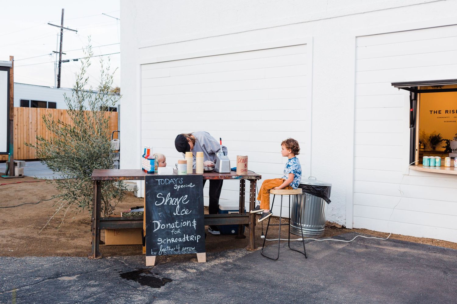 A line of customers wait at an outdoor coffee counter in a serene industrial space filled with natural light.