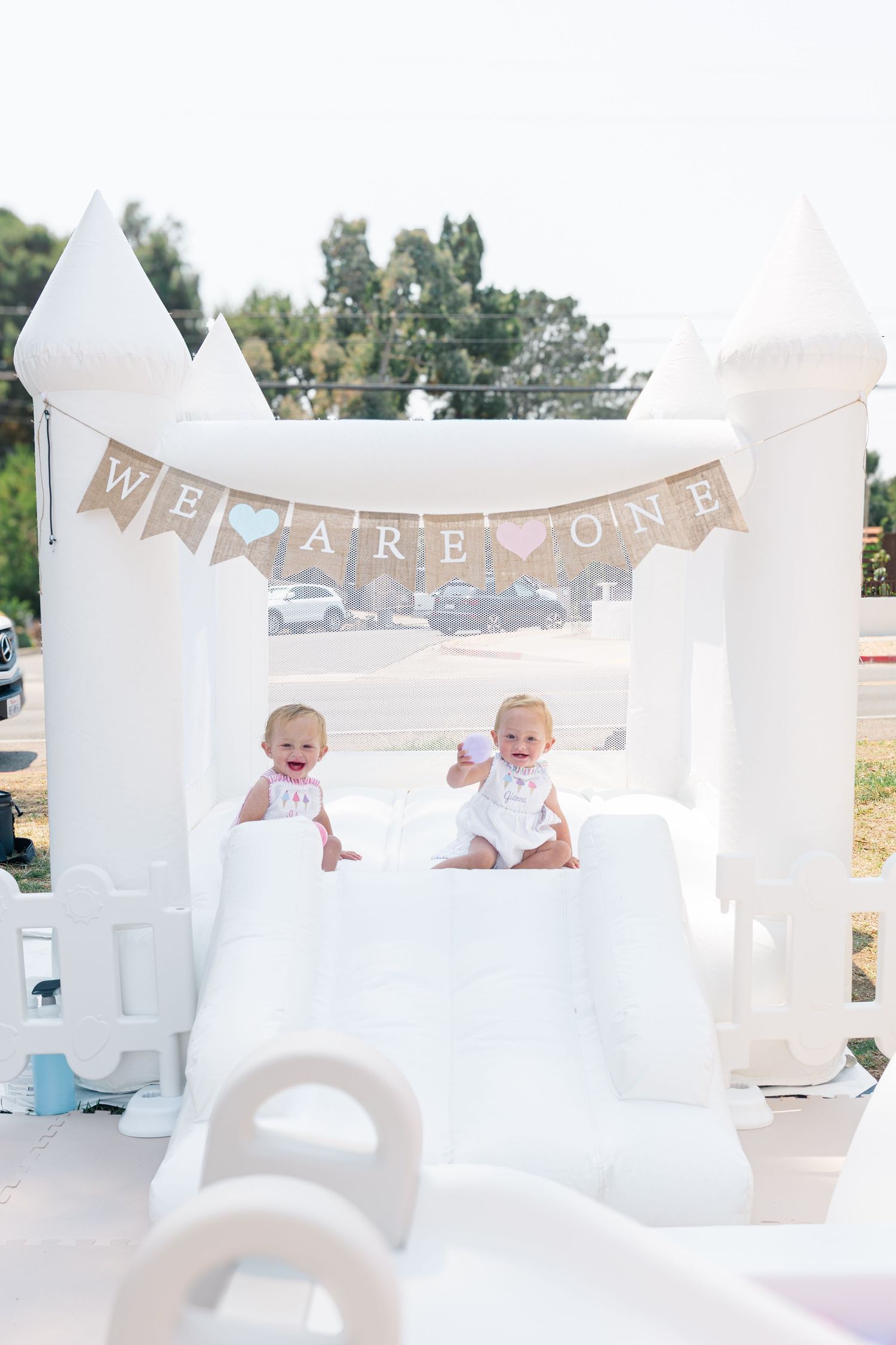 White party decorations and 'WE ARE ONE' banner displayed in bright outdoor setting.