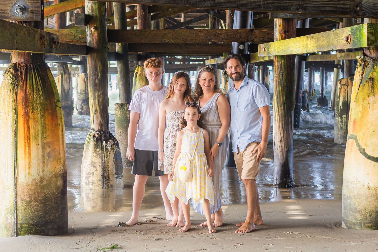 Group photo underneath wooden pier showing weathered posts and beams.