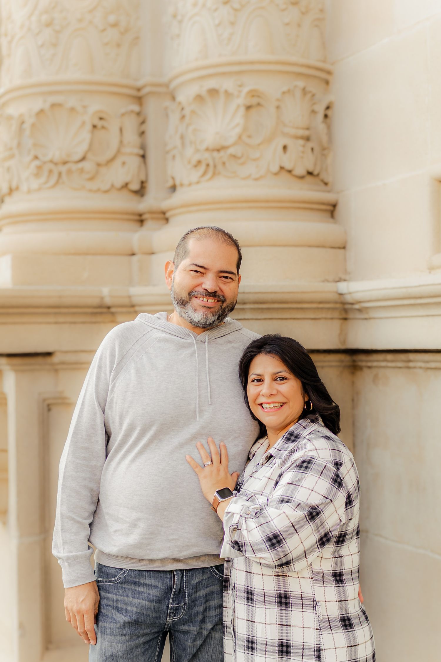 A couple shares joyful moments together while posing against ornate white columns in a romantic photoshoot.