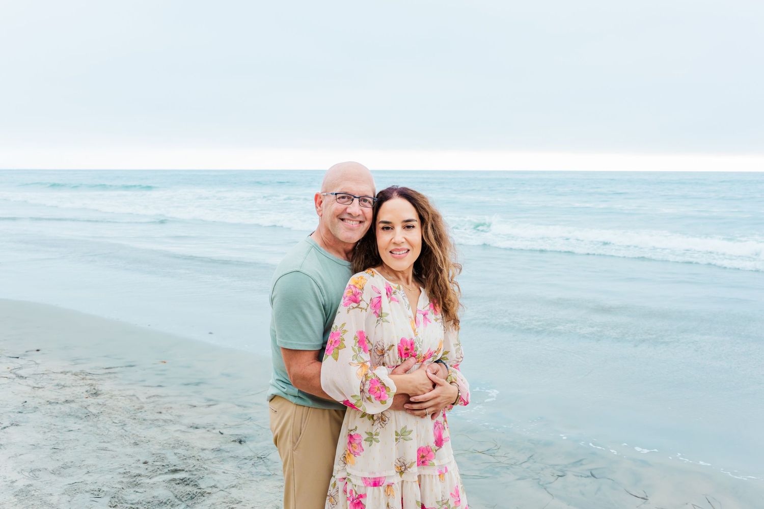A couple embraces on the beach with ocean waves in the background.