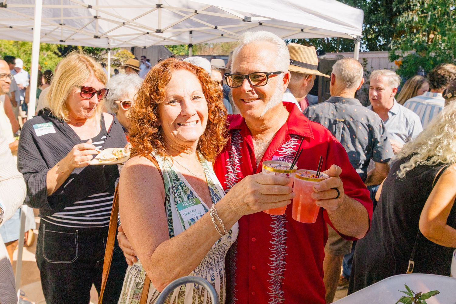 People laughing and celebrating at an outdoor party with white canopies overhead.