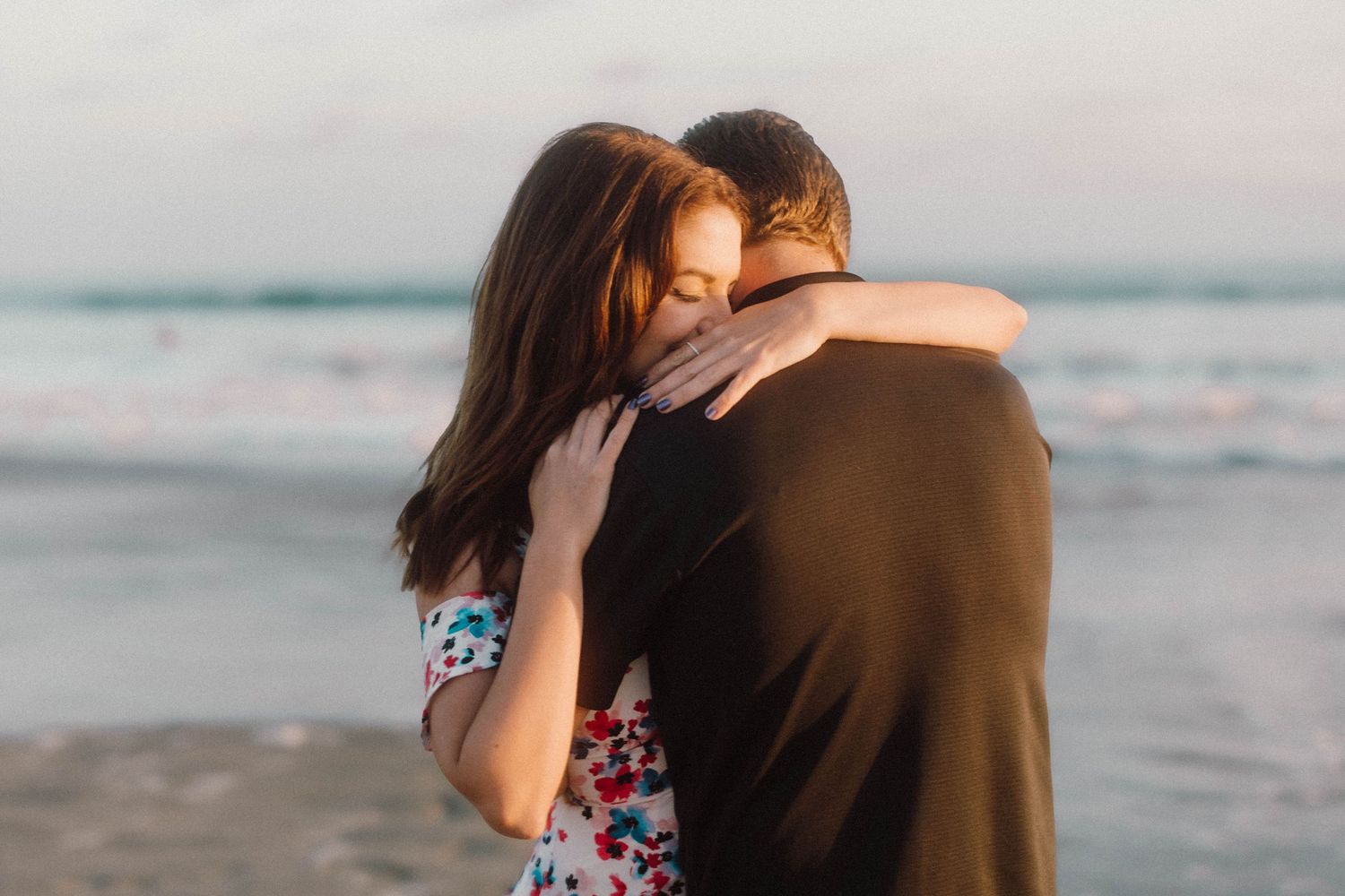 Couple sharing intimate moment on beach with ocean waves in background during golden hour.