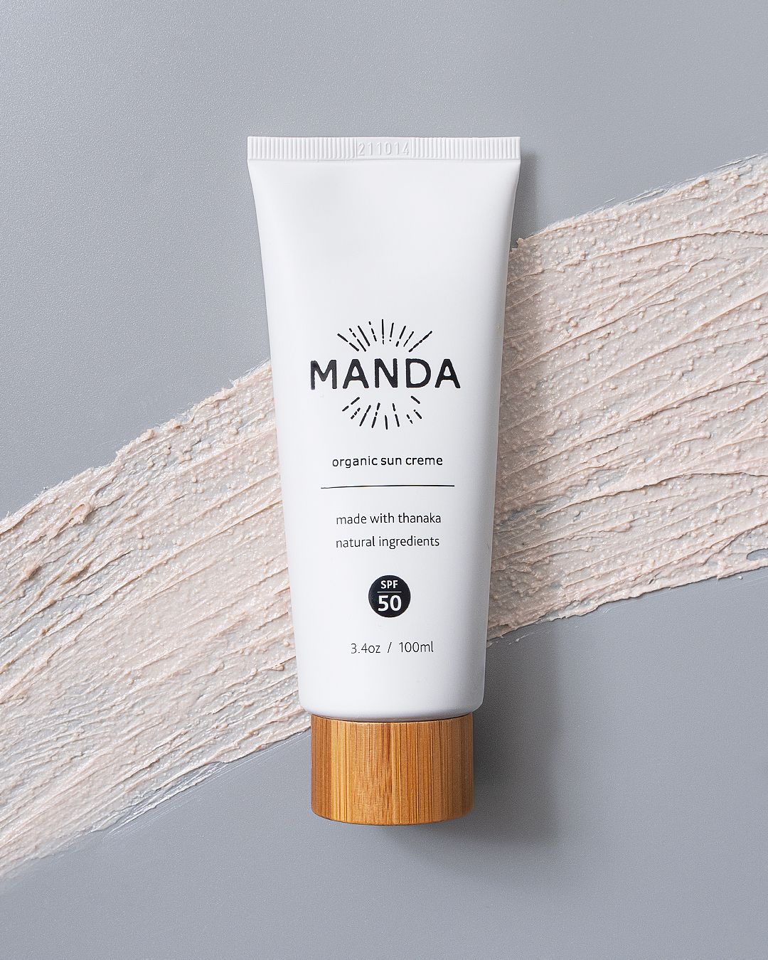 White Manda skincare tubes with wooden caps arranged on a textured grey and white surface.
