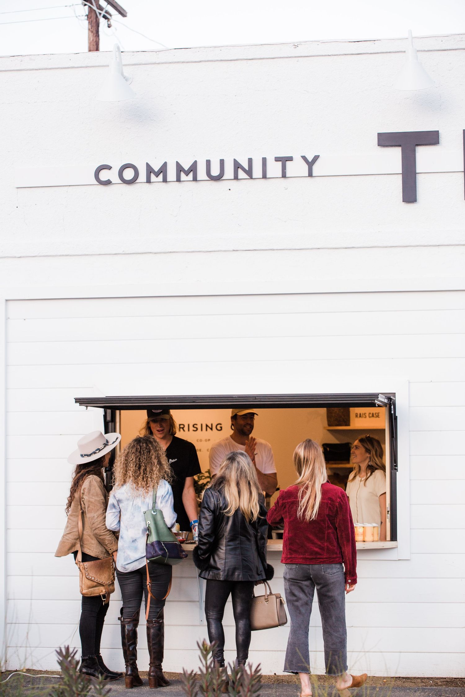 People waiting in line outside a white building with a community sign.