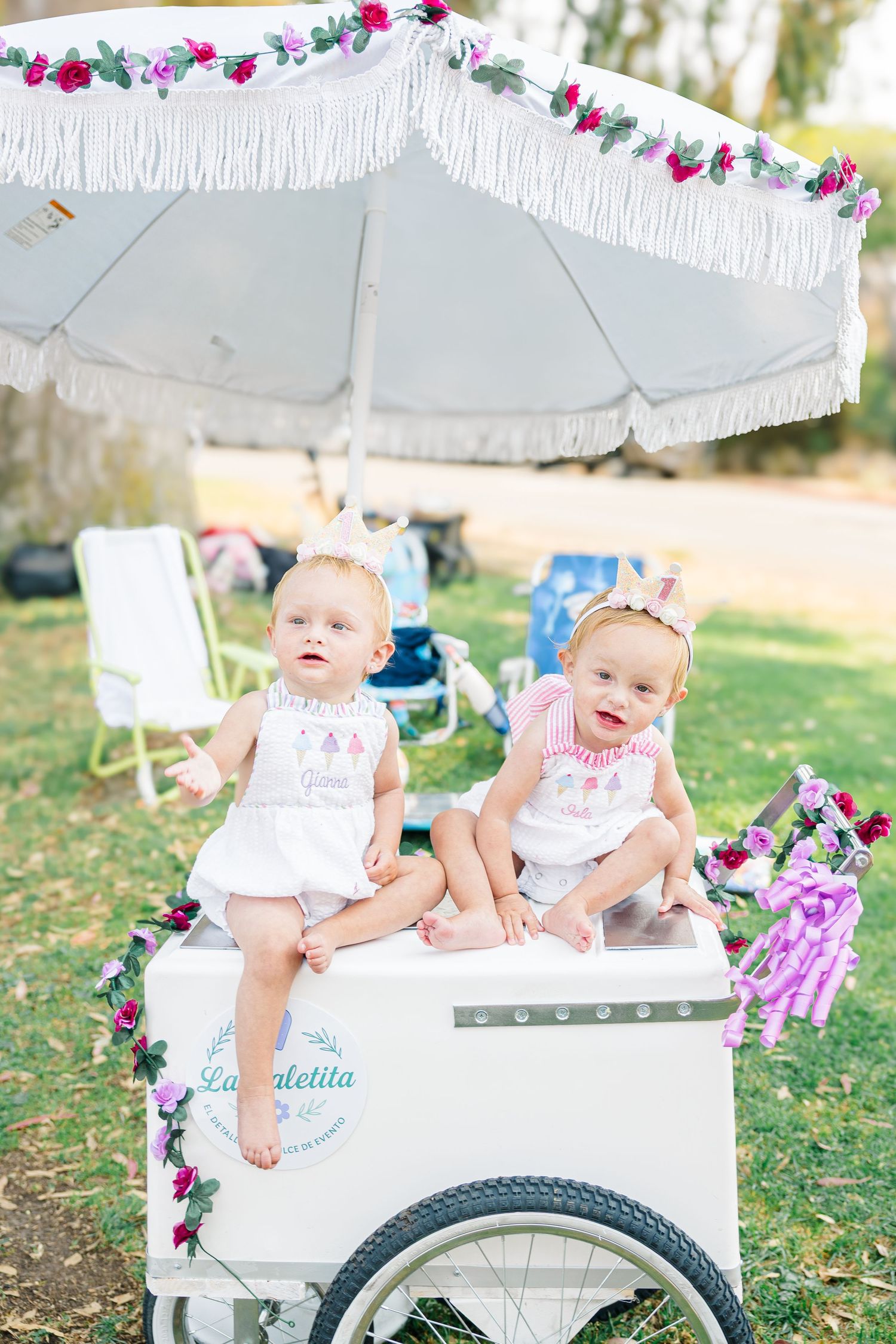 White decorative cart adorned with floral garlands at an outdoor celebration.