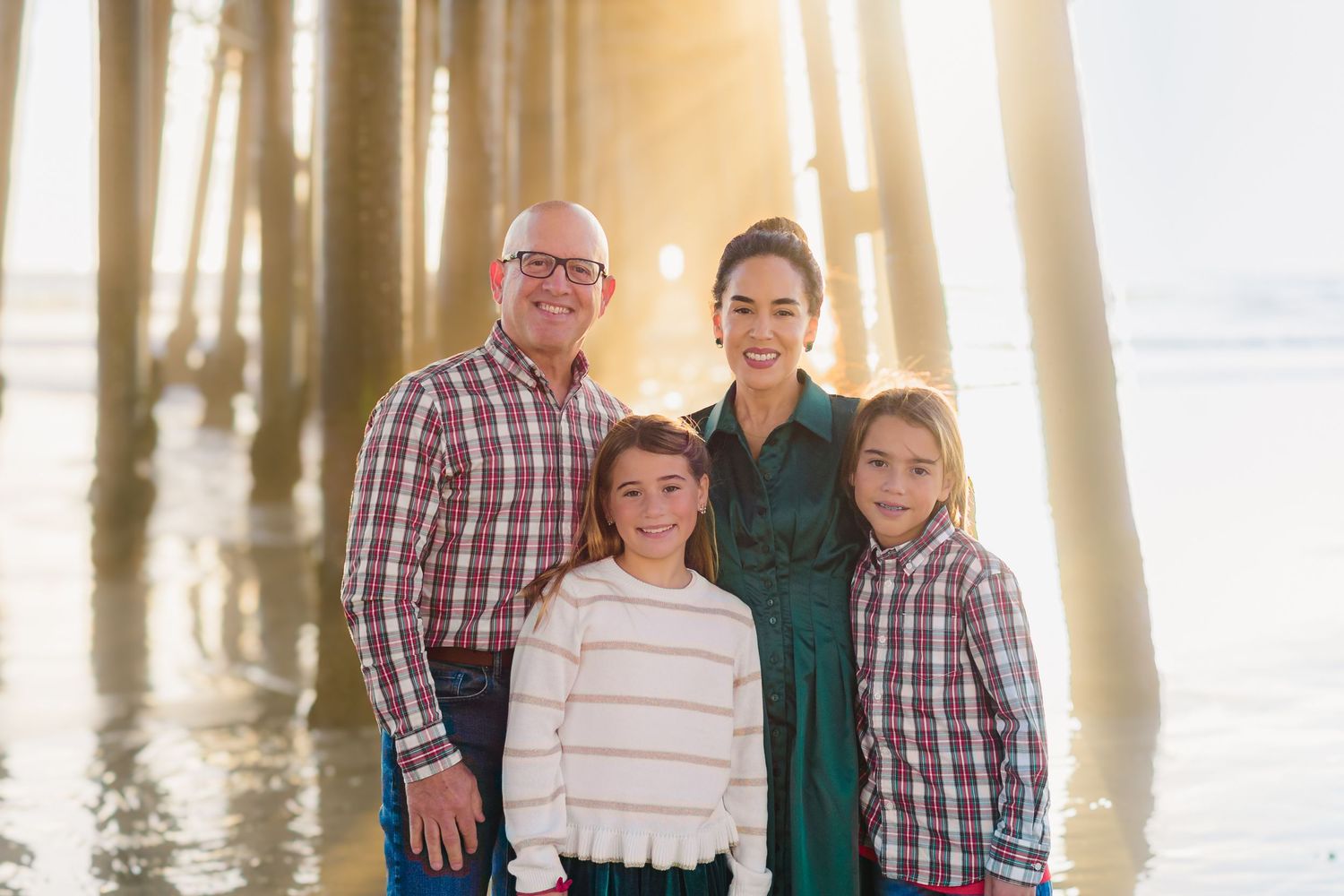 A multi-generational family poses together on a beach at sunset with a wooden pier in the background.