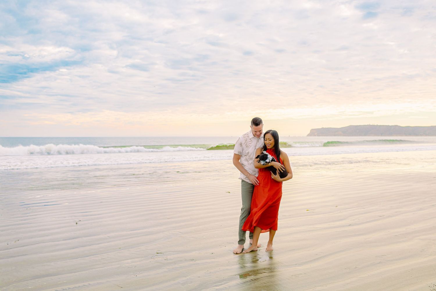 A couple walks along a scenic beach at sunset holding hands and splashing in the shallow ocean waves.