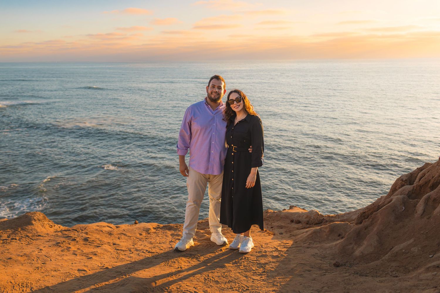 Couple shares a romantic moment on coastal cliffs during golden sunset over the ocean.