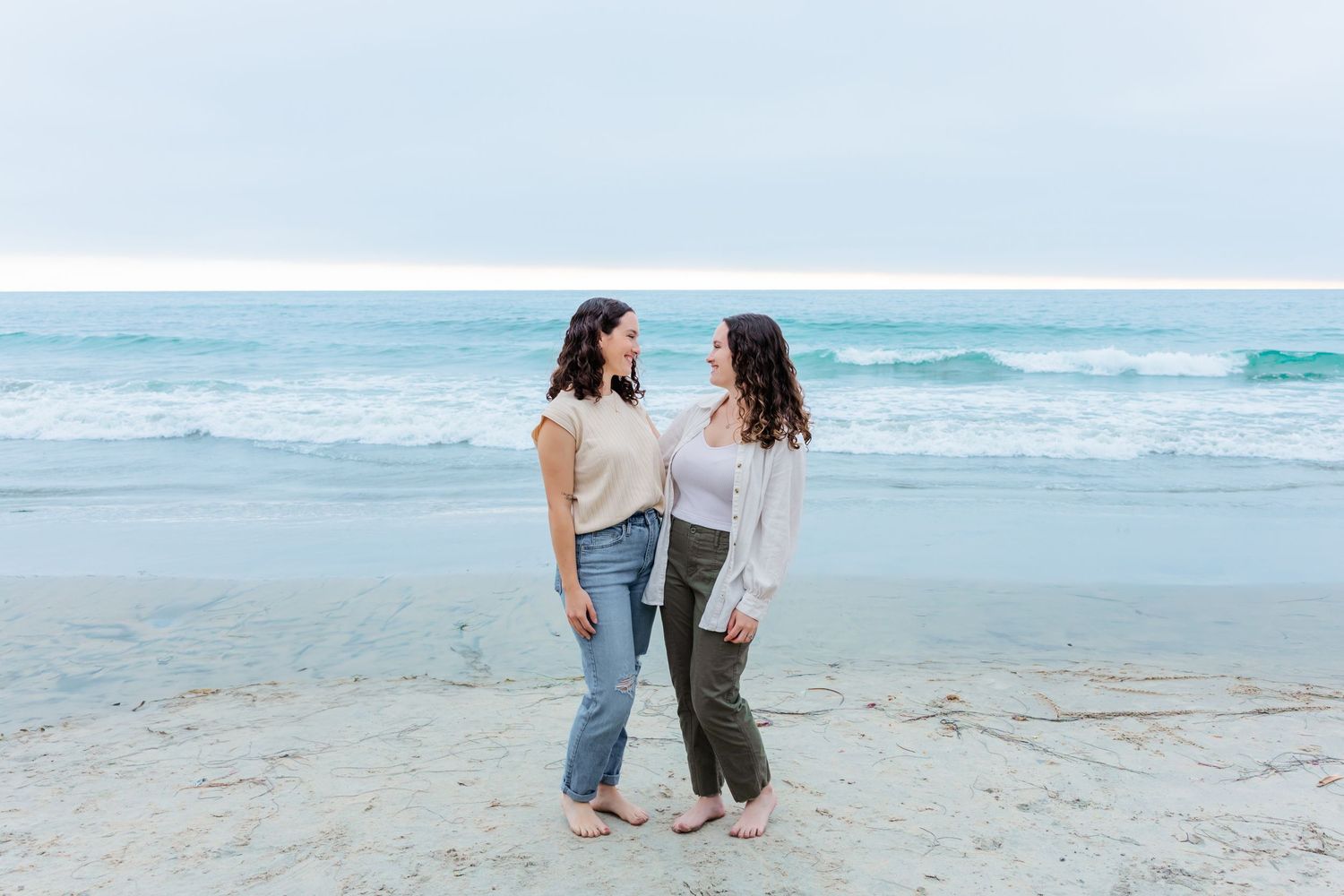 Two people walk together on a peaceful beach during an overcast day.