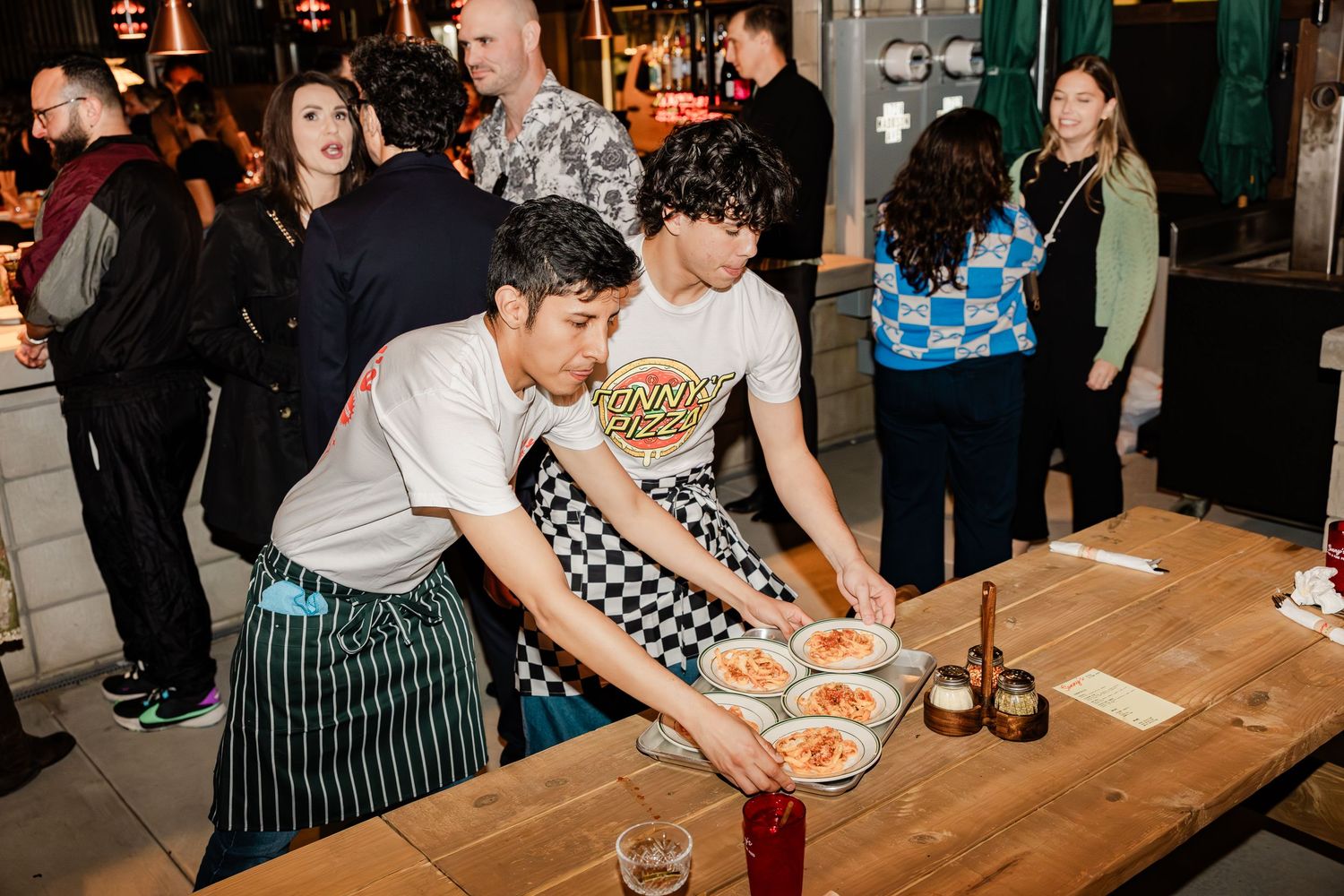 Restaurant staff preparing and plating dishes on a long wooden table during service.