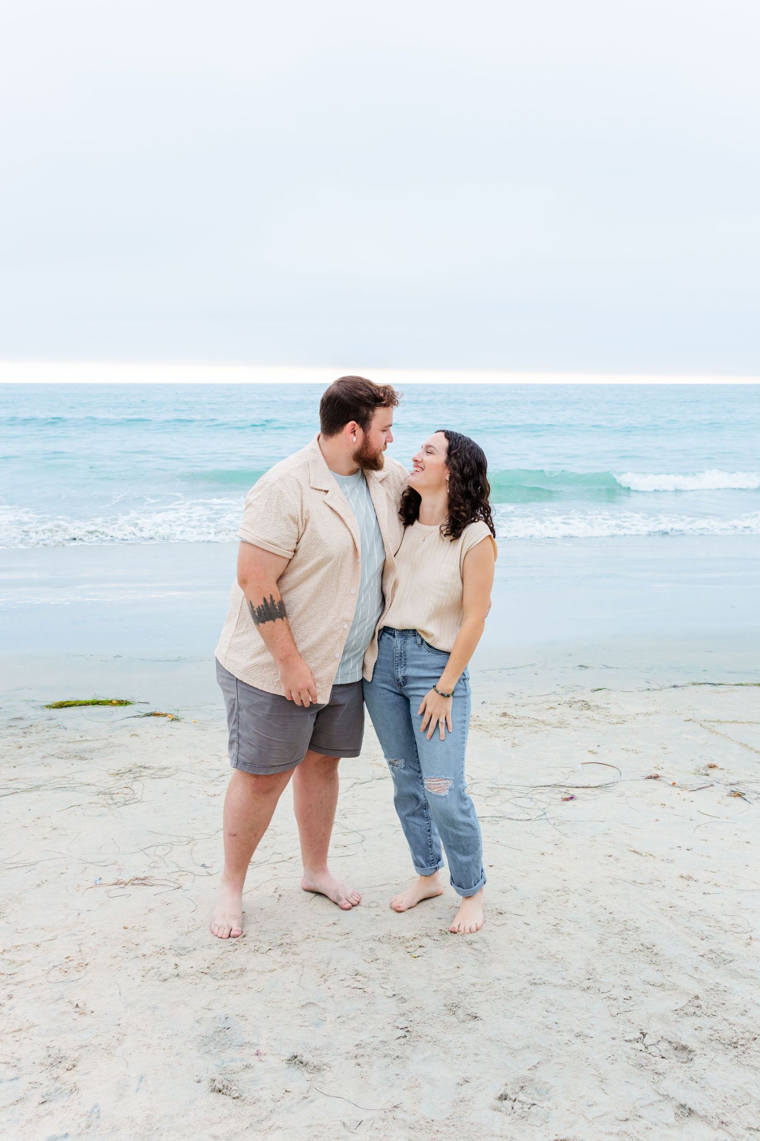 A couple shares a romantic moment on a peaceful beach with ocean waves in the background.