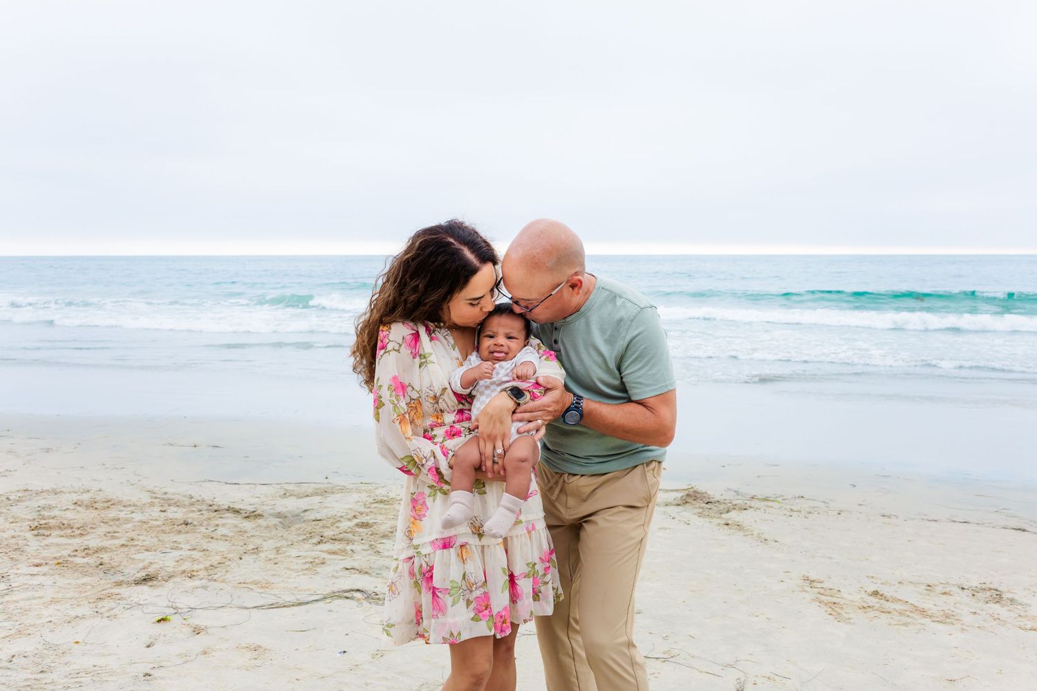 Three people share intimate moment on beach with ocean waves behind them.