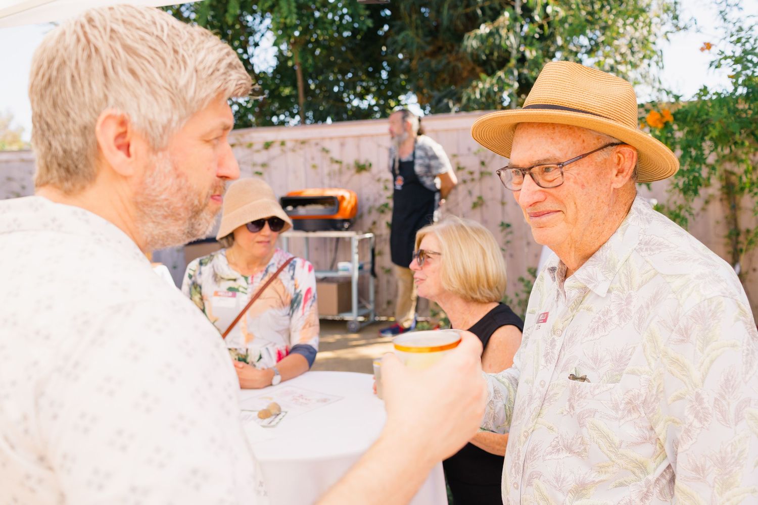 Guests mingling at a casual outdoor party with yellow patio umbrellas.
