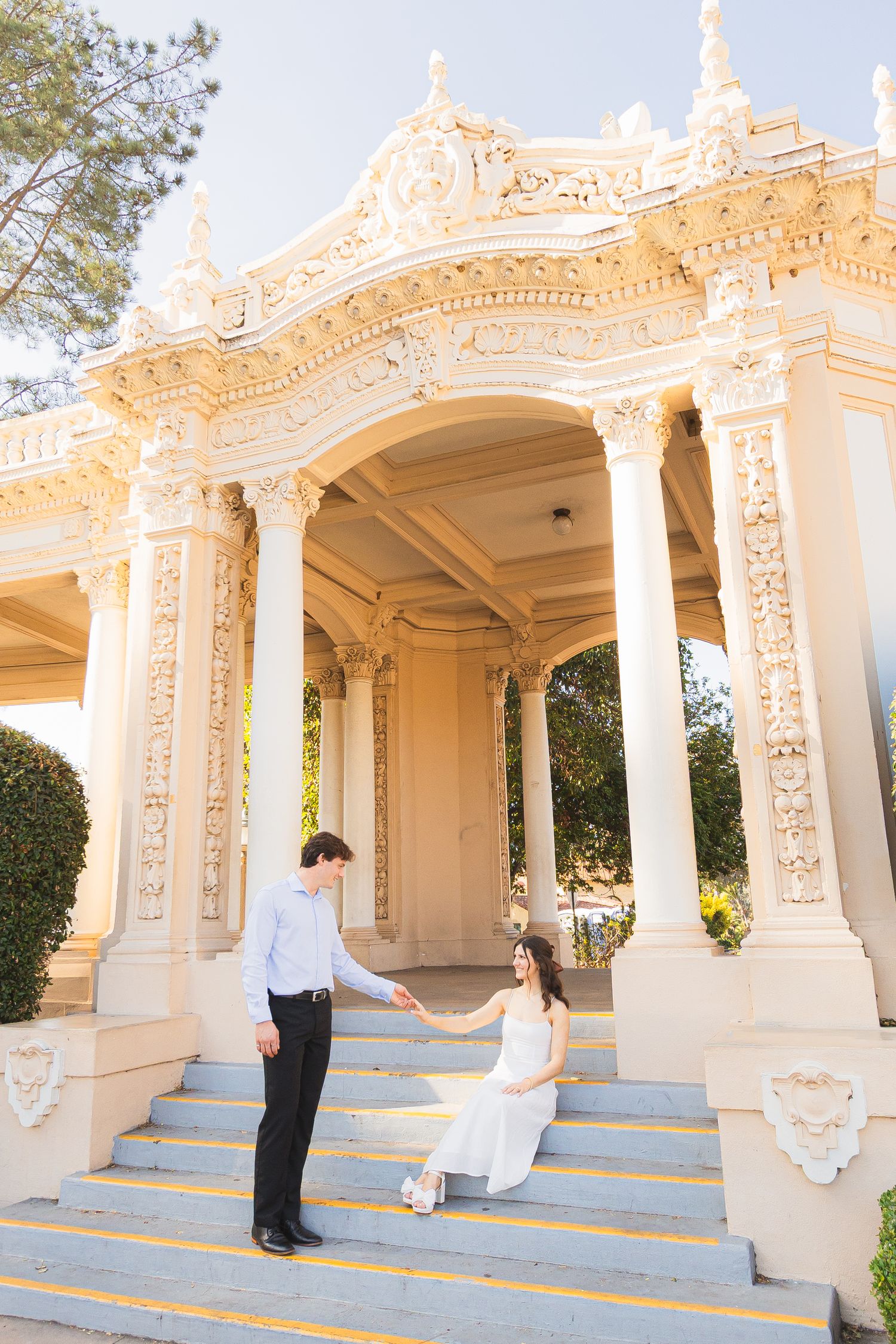Elegant white ornate gazebo with decorative columns and blue steps in warm sunlight at a garden venue.