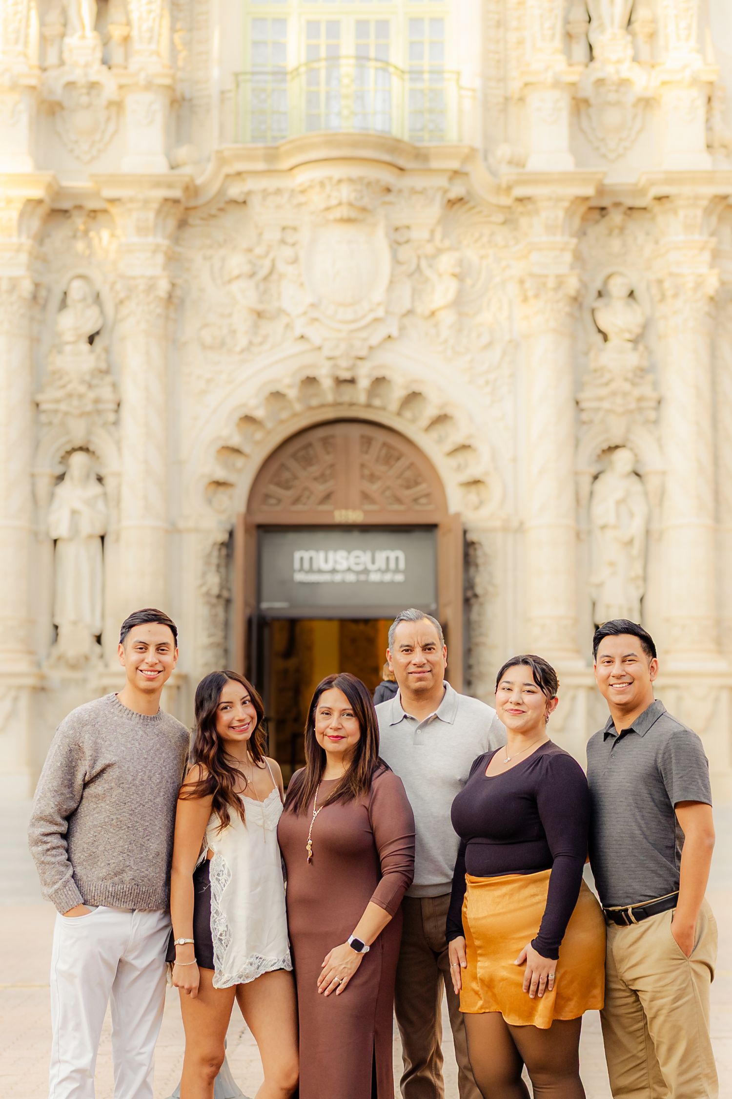 A diverse group poses together against an ornate museum facade with decorative columns and archways.